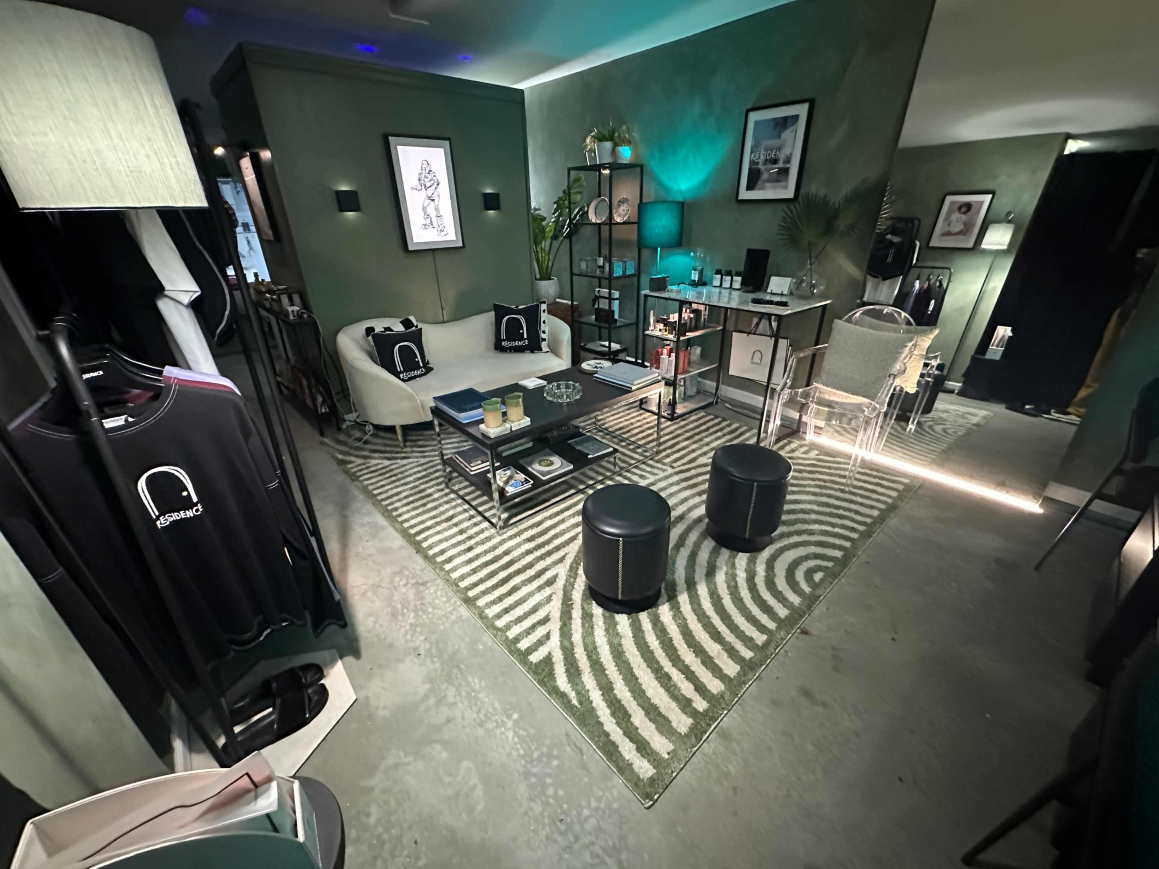 The image shows a stylish living space featuring a green wall, a comfortable sofa, a coffee table surrounded by two small stools, and various decorative items.