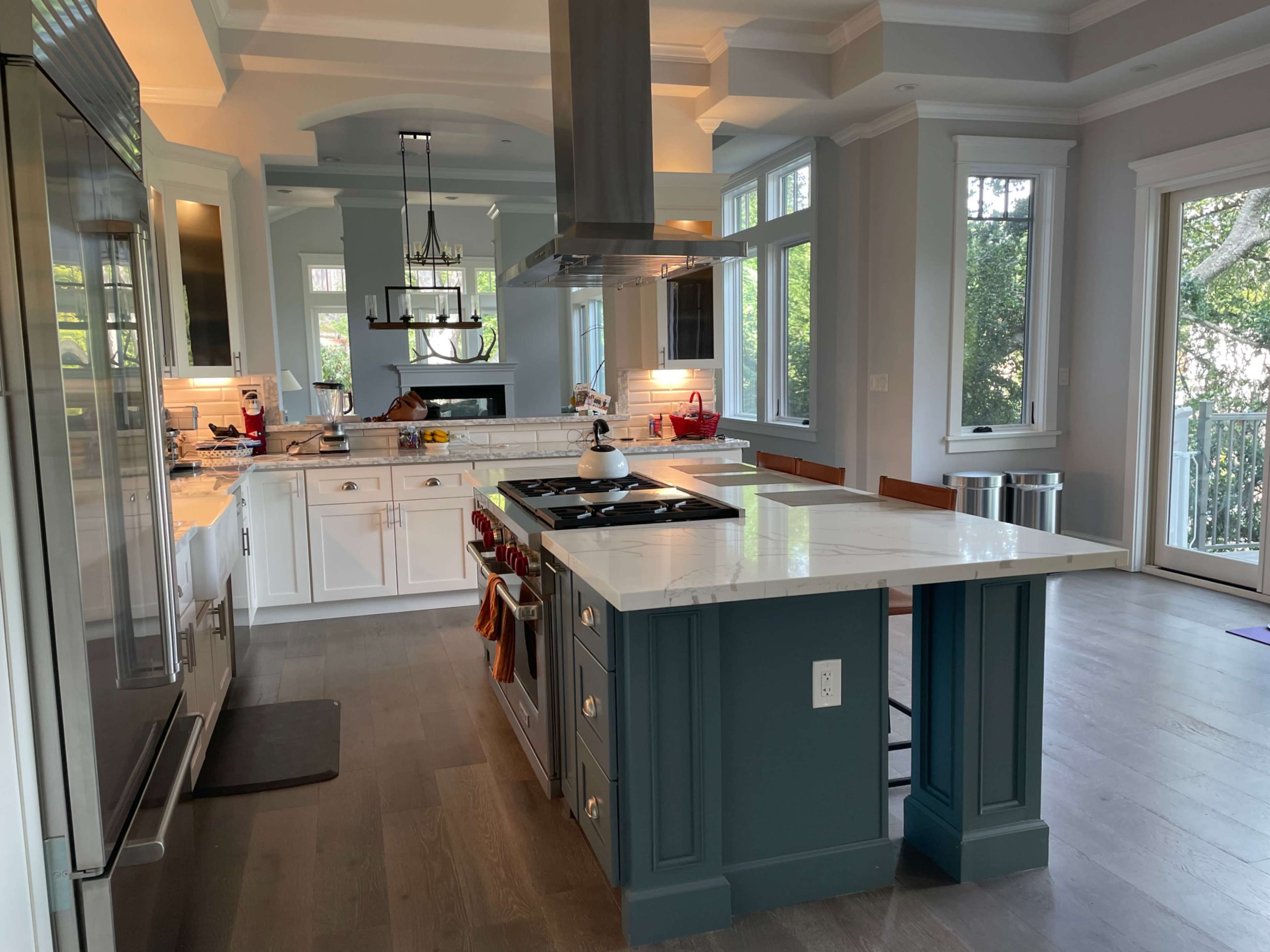A spacious kitchen features a large island with a marble countertop, stainless steel appliances, and multiple windows providing natural light.