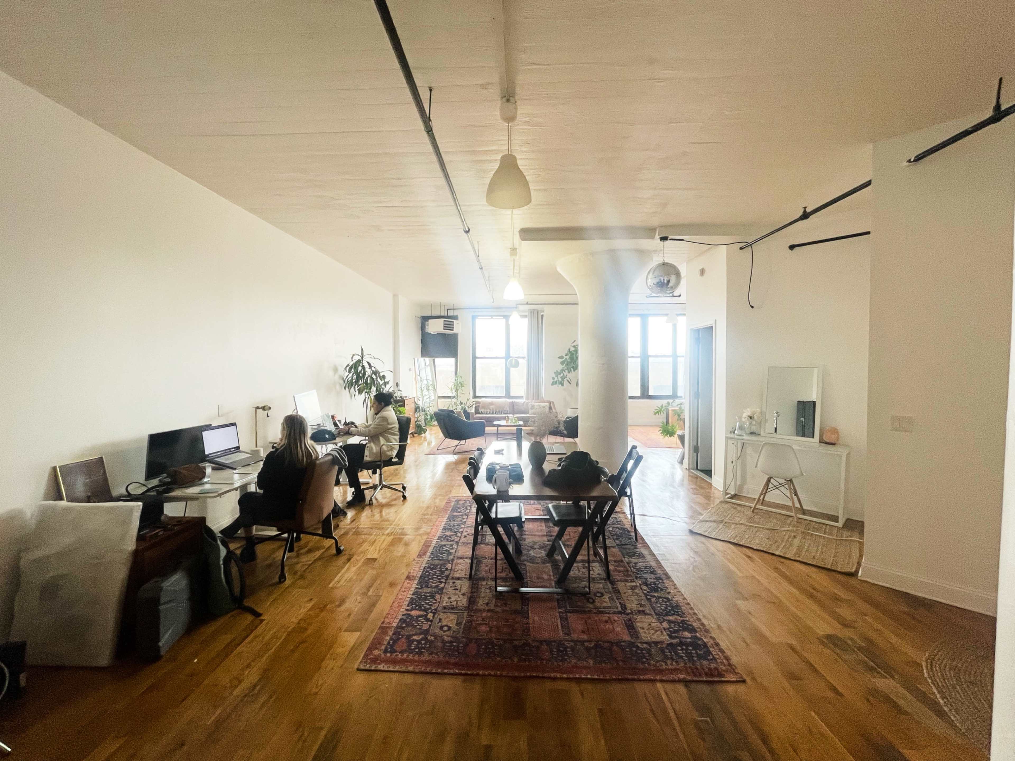 A spacious, modern office space features multiple workstations, a lounge area, and large windows letting in natural light.