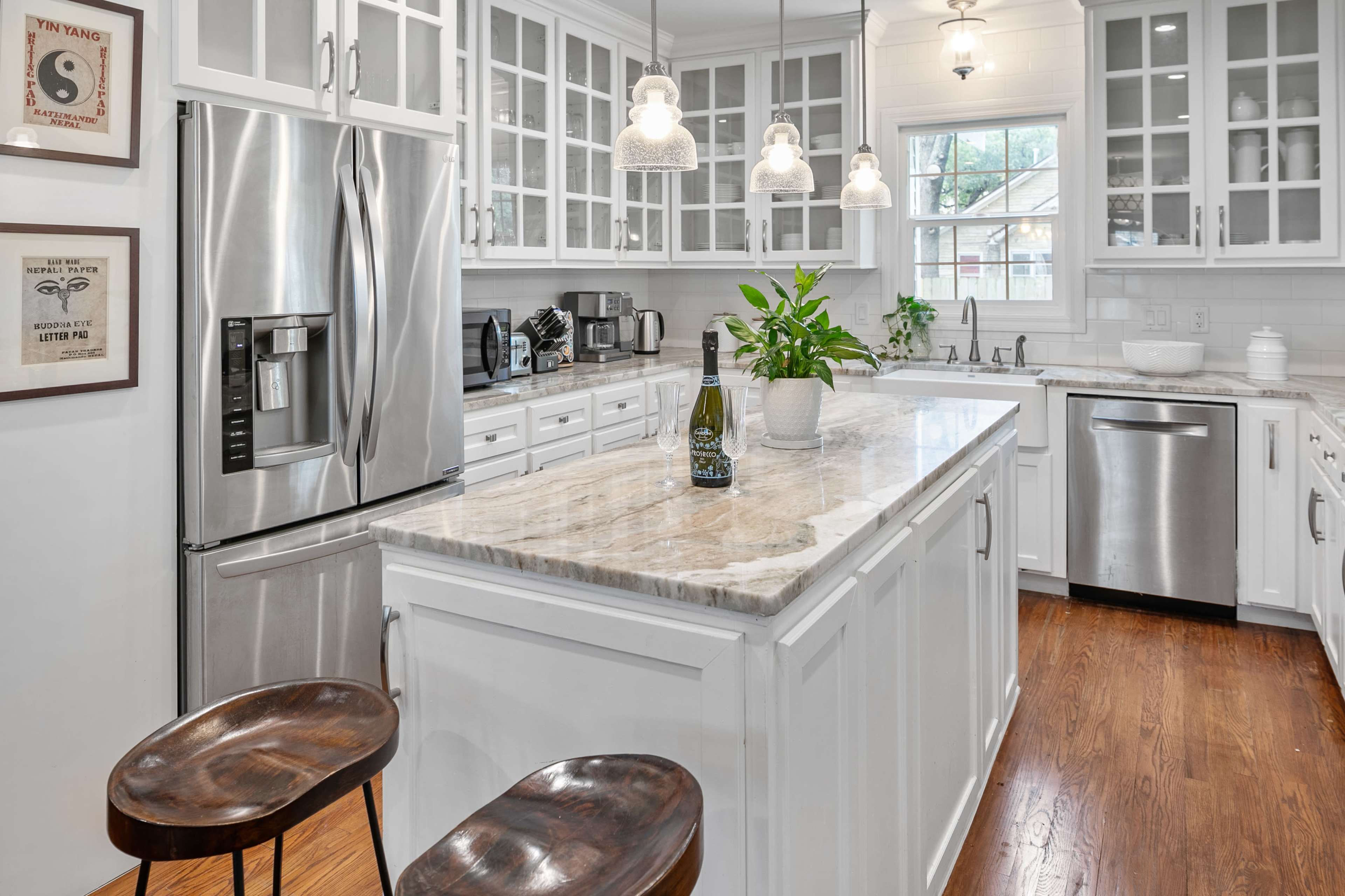 A modern kitchen with white cabinetry, a large marble island, a stainless steel refrigerator, and wooden stools.
