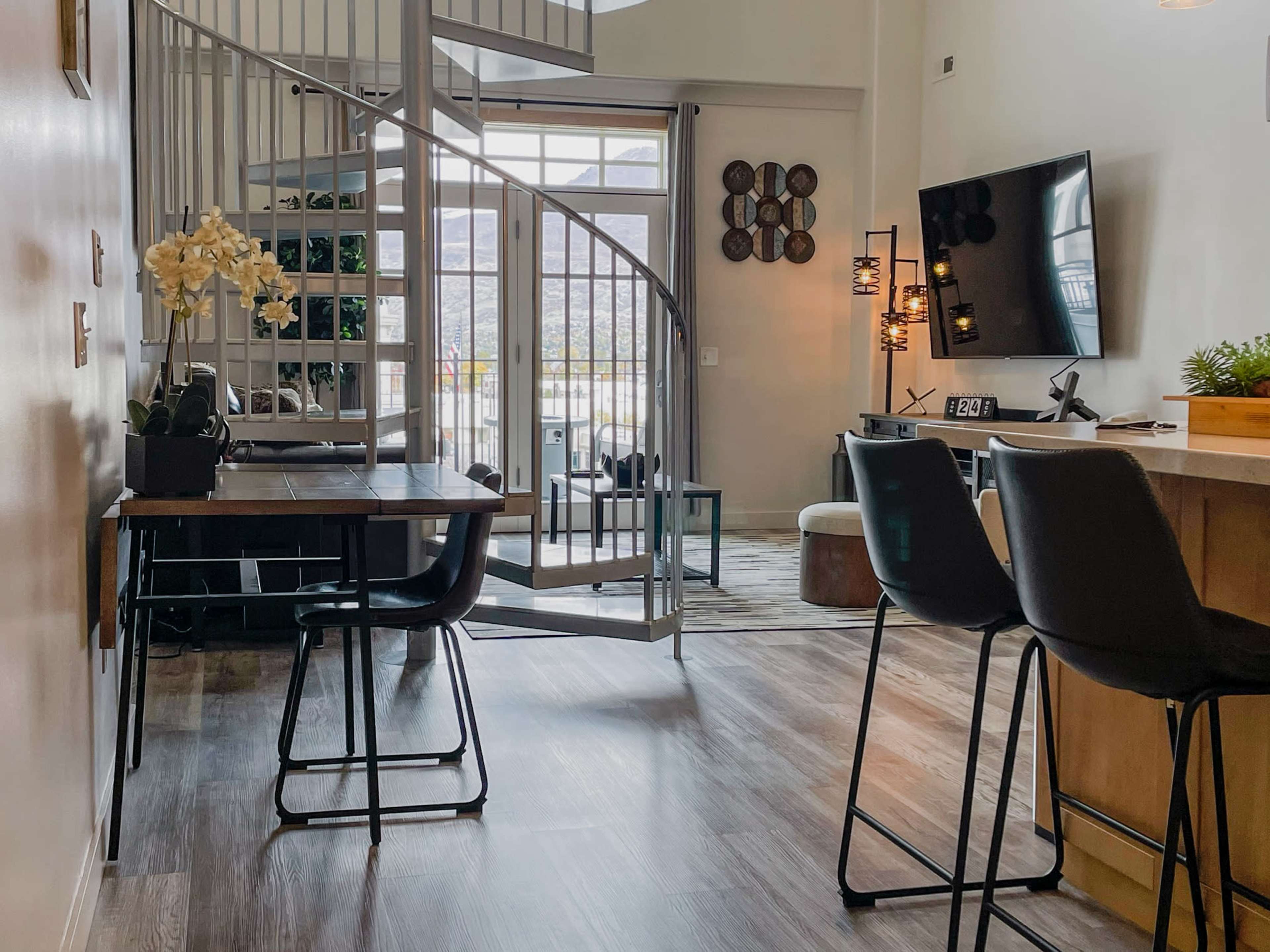 A modern living space features a spiral staircase, a wooden dining table, and a television mounted on the wall.