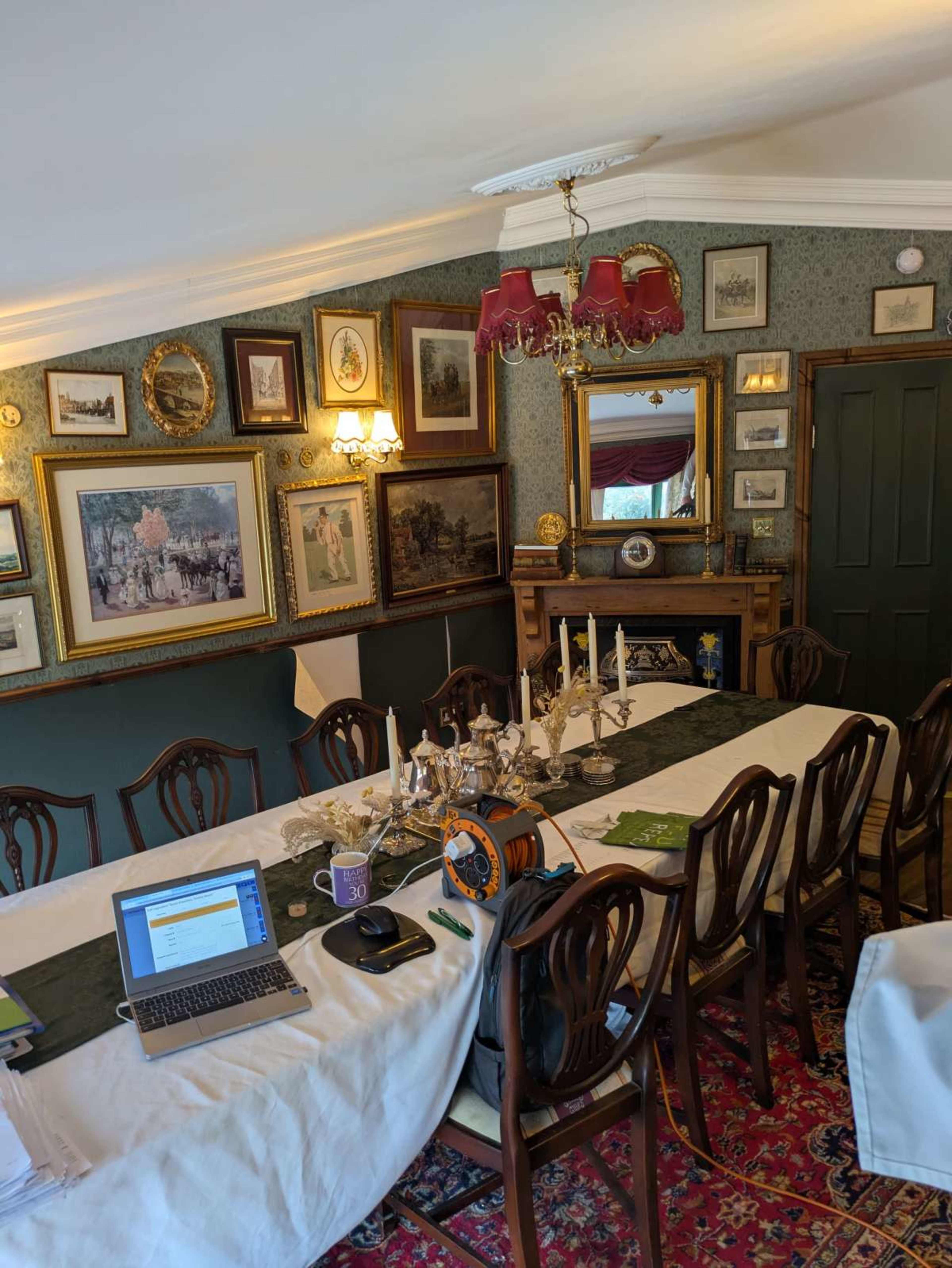 A long dining table is set in a decorated room filled with framed artworks and a chandelier.