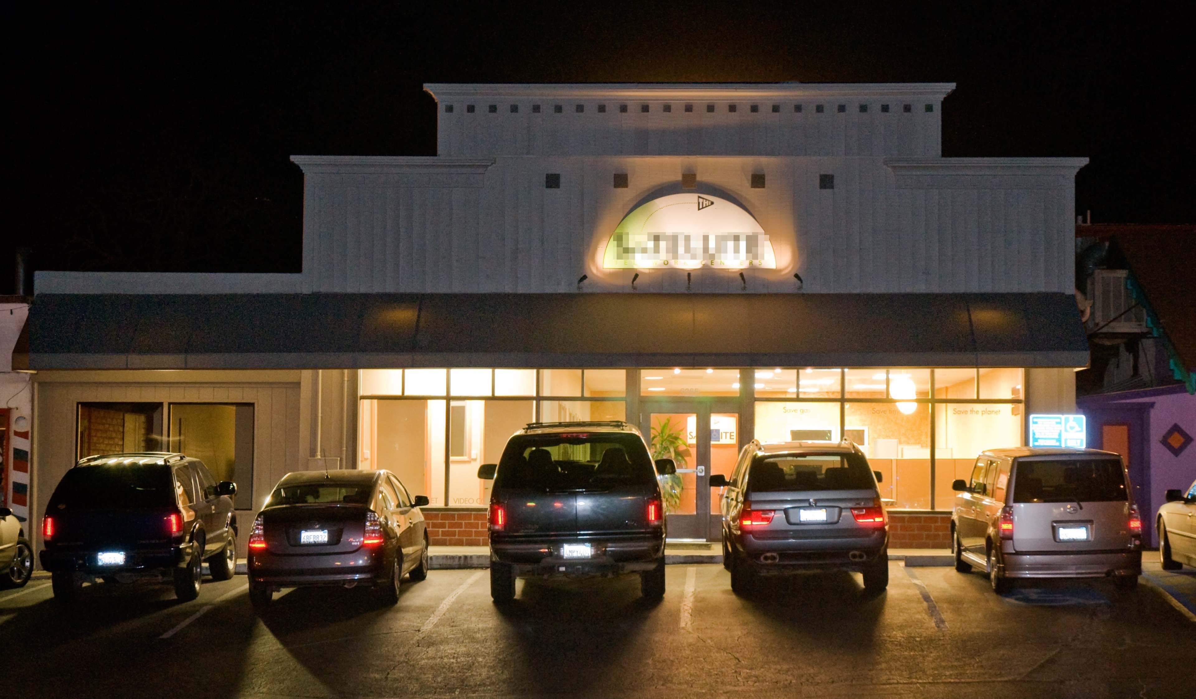 A row of vehicles is parked in front of a well-lit commercial building at night, featuring large windows and the name "LITHIUM" displayed prominently.