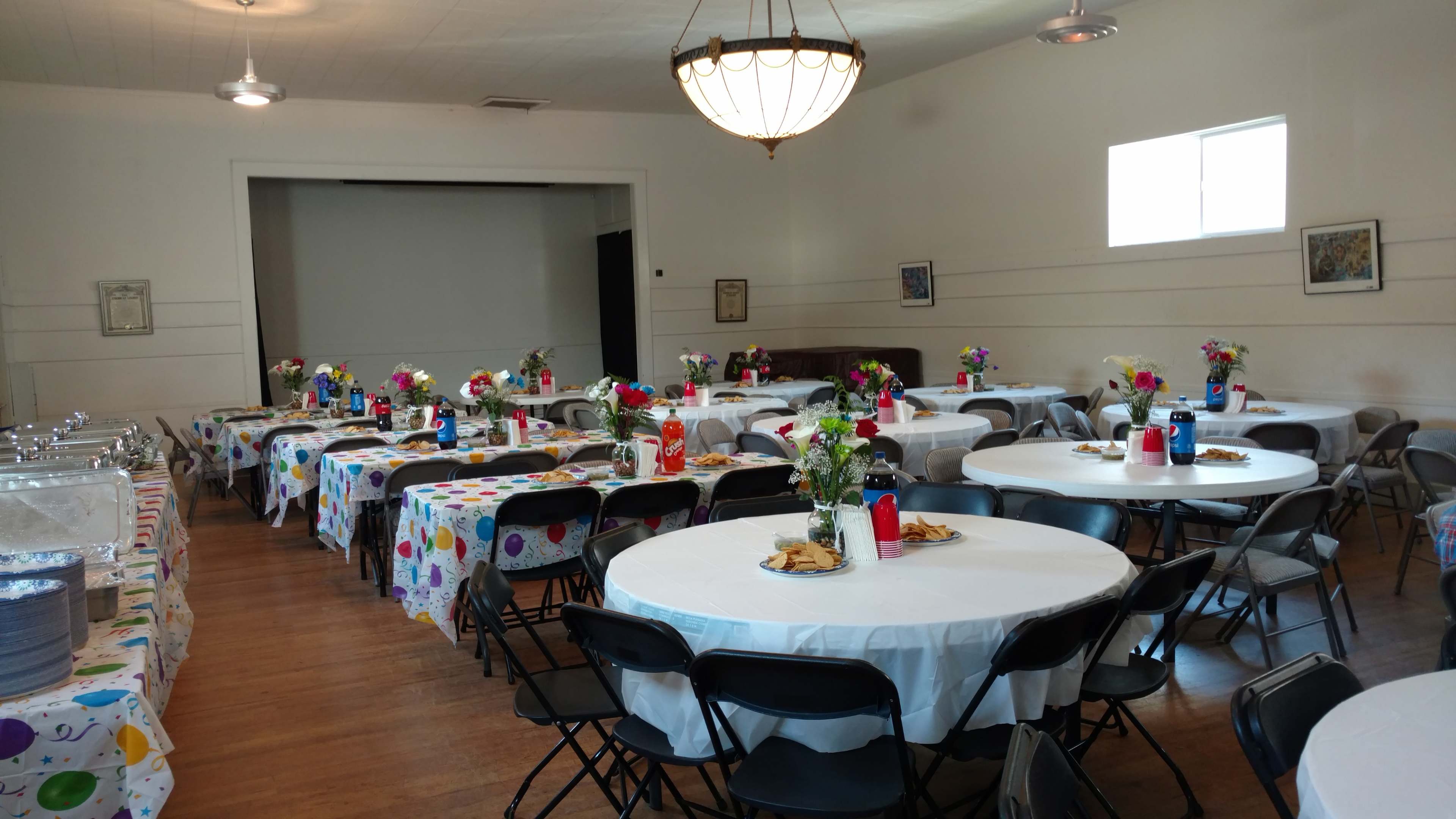 The image shows a spacious banquet hall arranged with several round tables covered in polka-dotted tablecloths, each set with floral centerpieces and place settings.