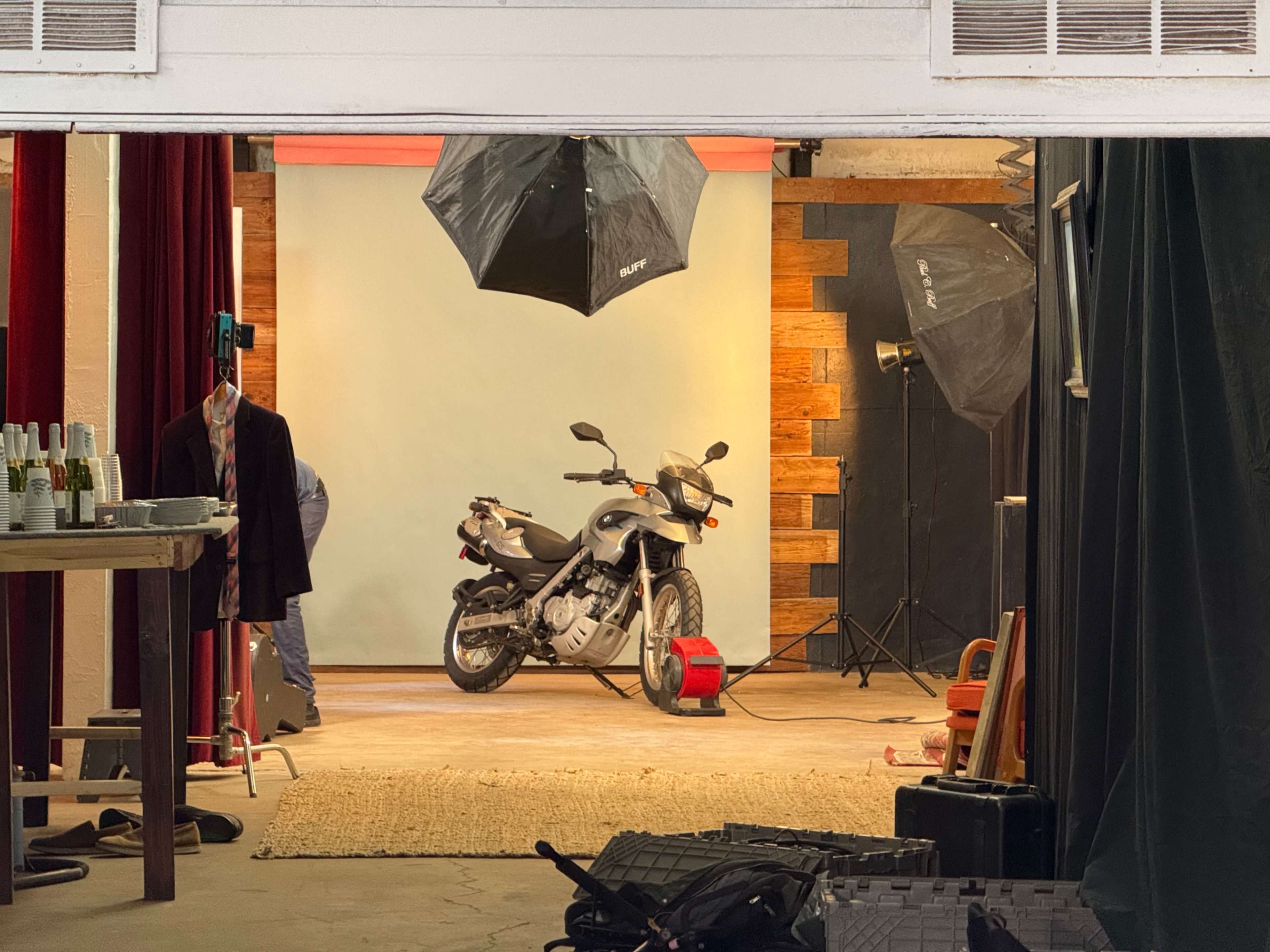 A motorcycle is positioned on a carpet in a studio setting with photography lights and backdrops.