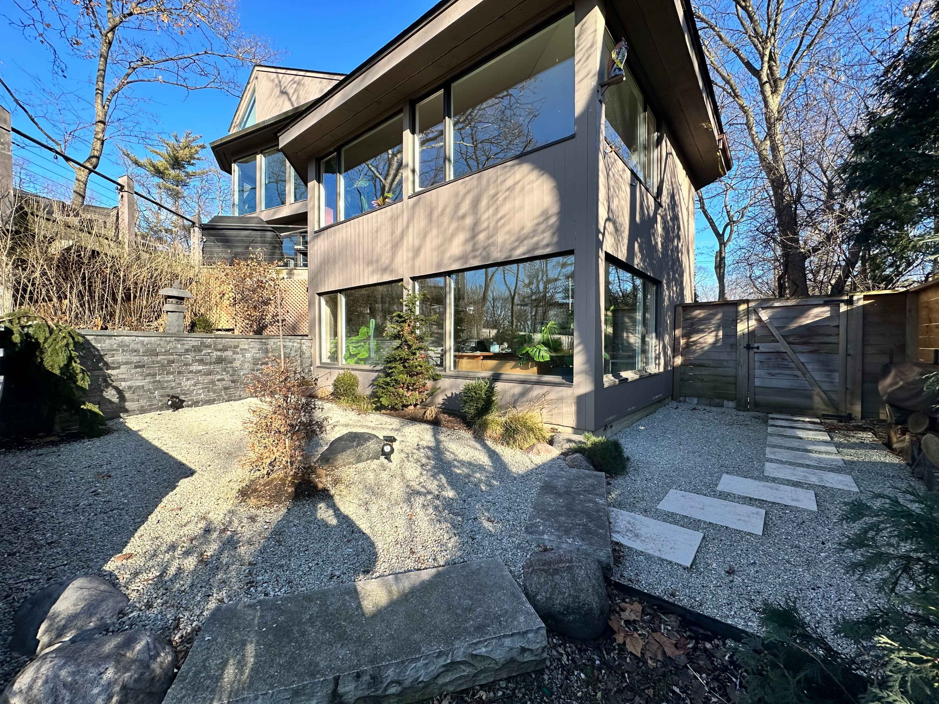 A modern house with large windows, surrounded by a landscaped garden featuring gravel pathways and decorative rocks.