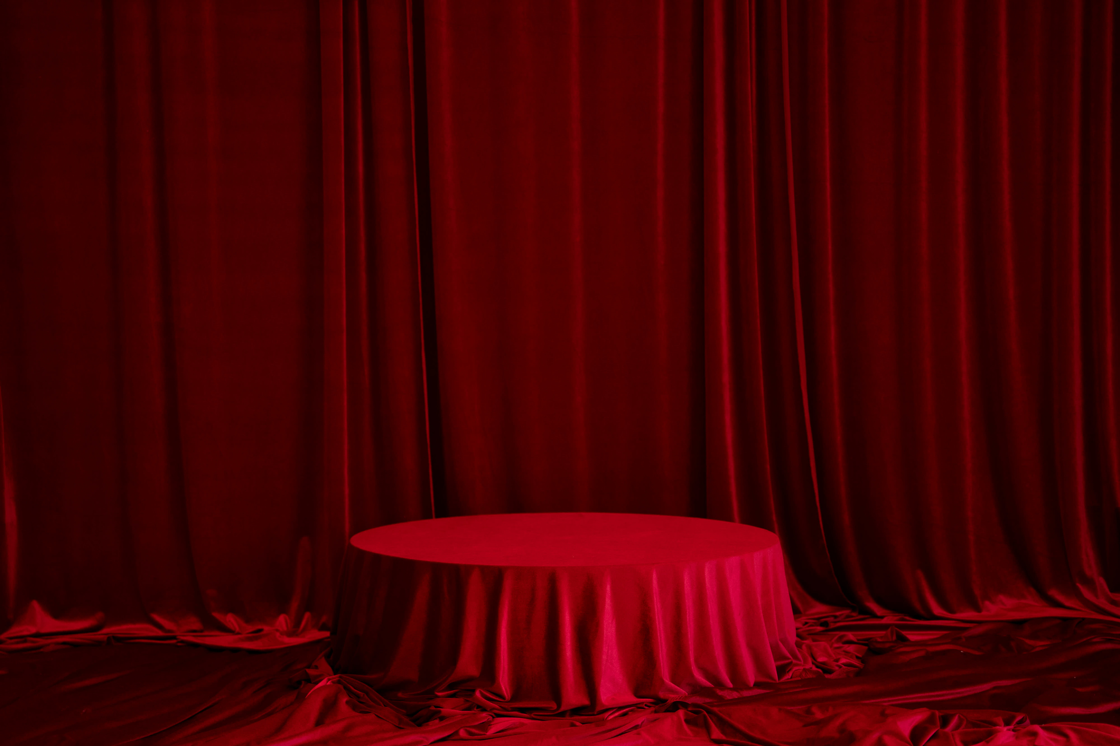 A circular table covered with a red cloth is set against a background of red draped fabric.