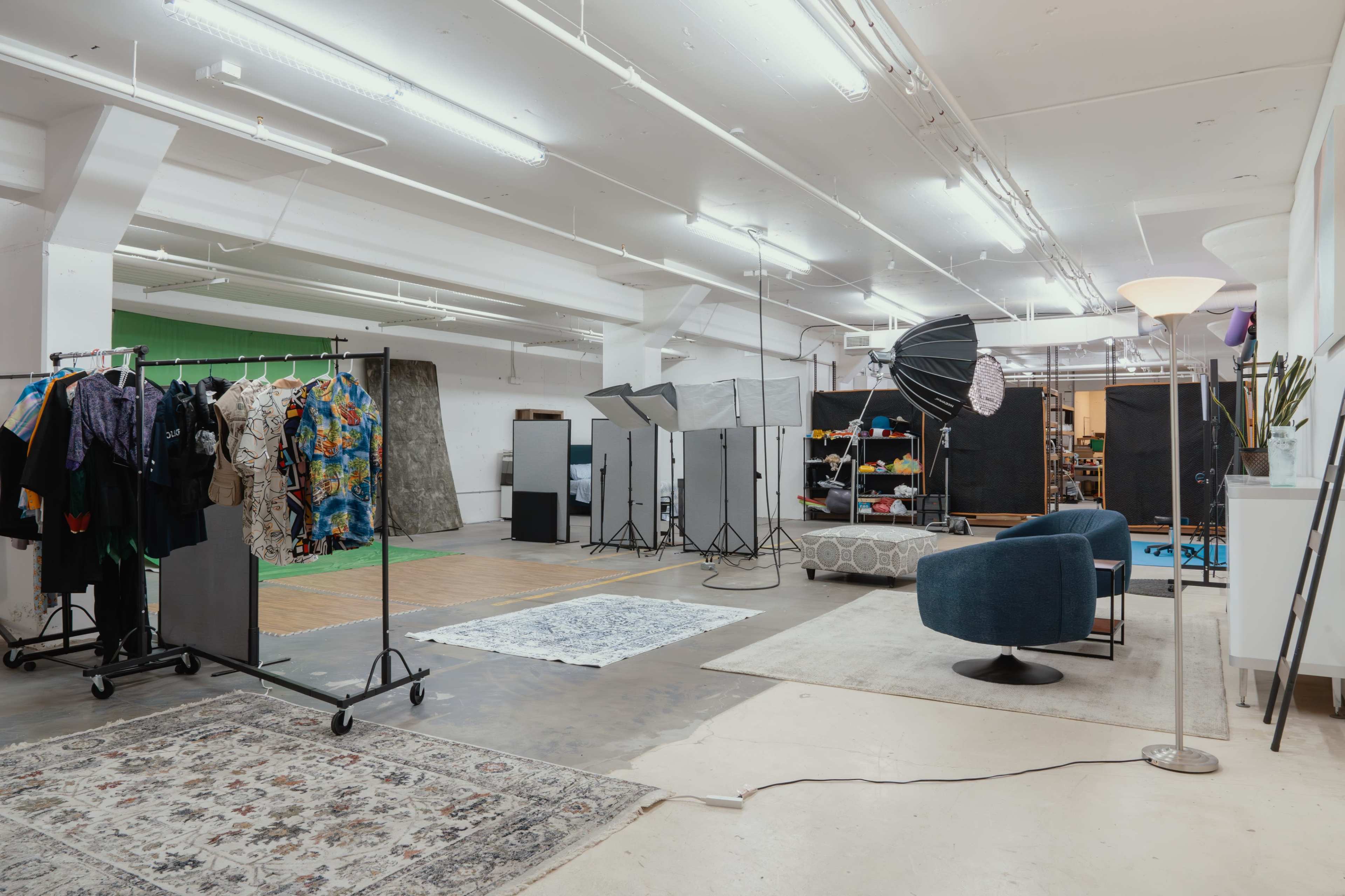 The image shows a spacious photography studio featuring clothing racks, backdrops, lighting equipment, and seating arrangements.