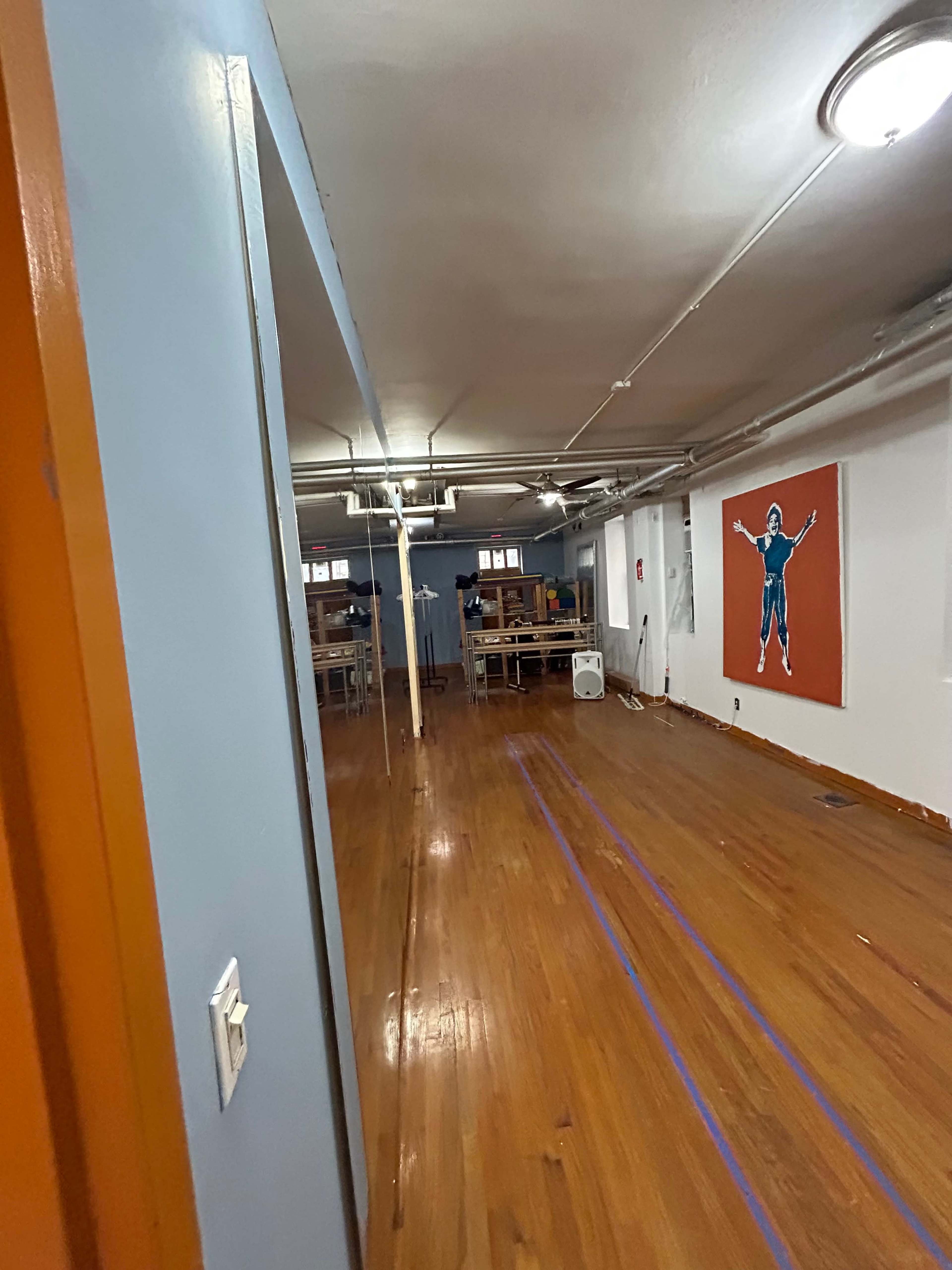A partially renovated interior space with wooden floors, blue walls, and a large artwork on an orange background.