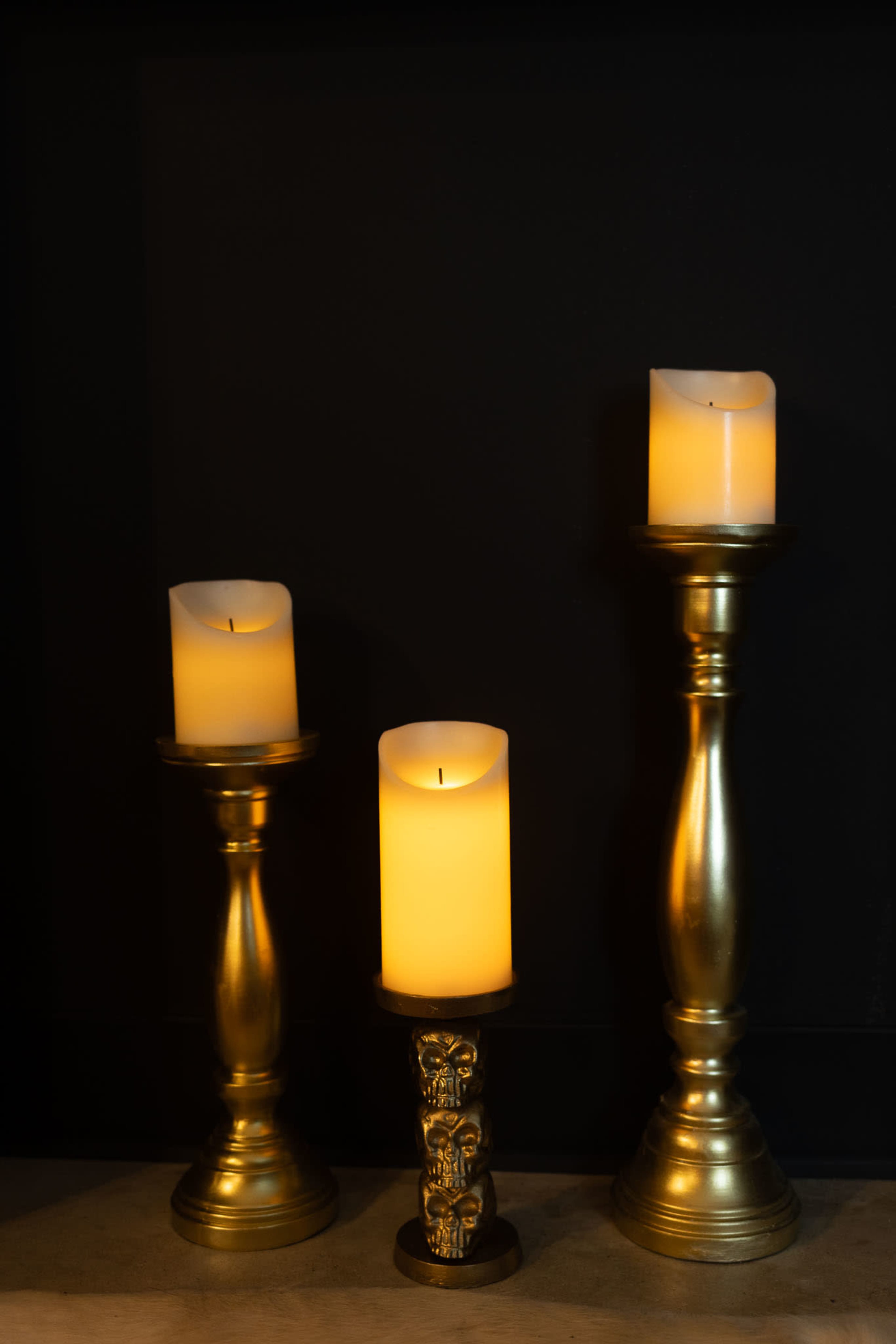 Three decorative candles with warm yellow flames are placed on ornate golden candle holders against a black background.