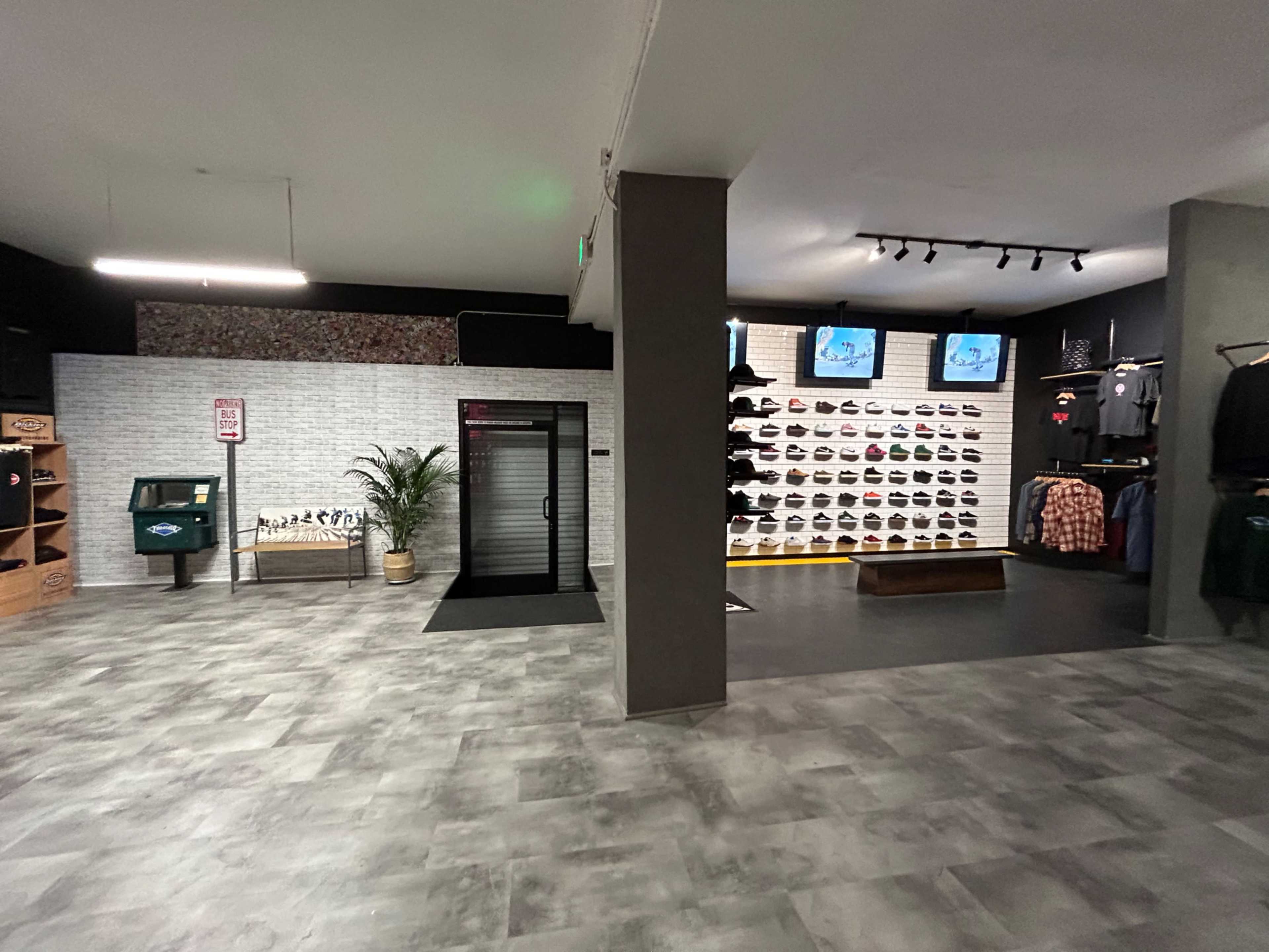 The interior of a retail store featuring a wall of displayed shoes, clothing racks, and a cash register area with a security door.