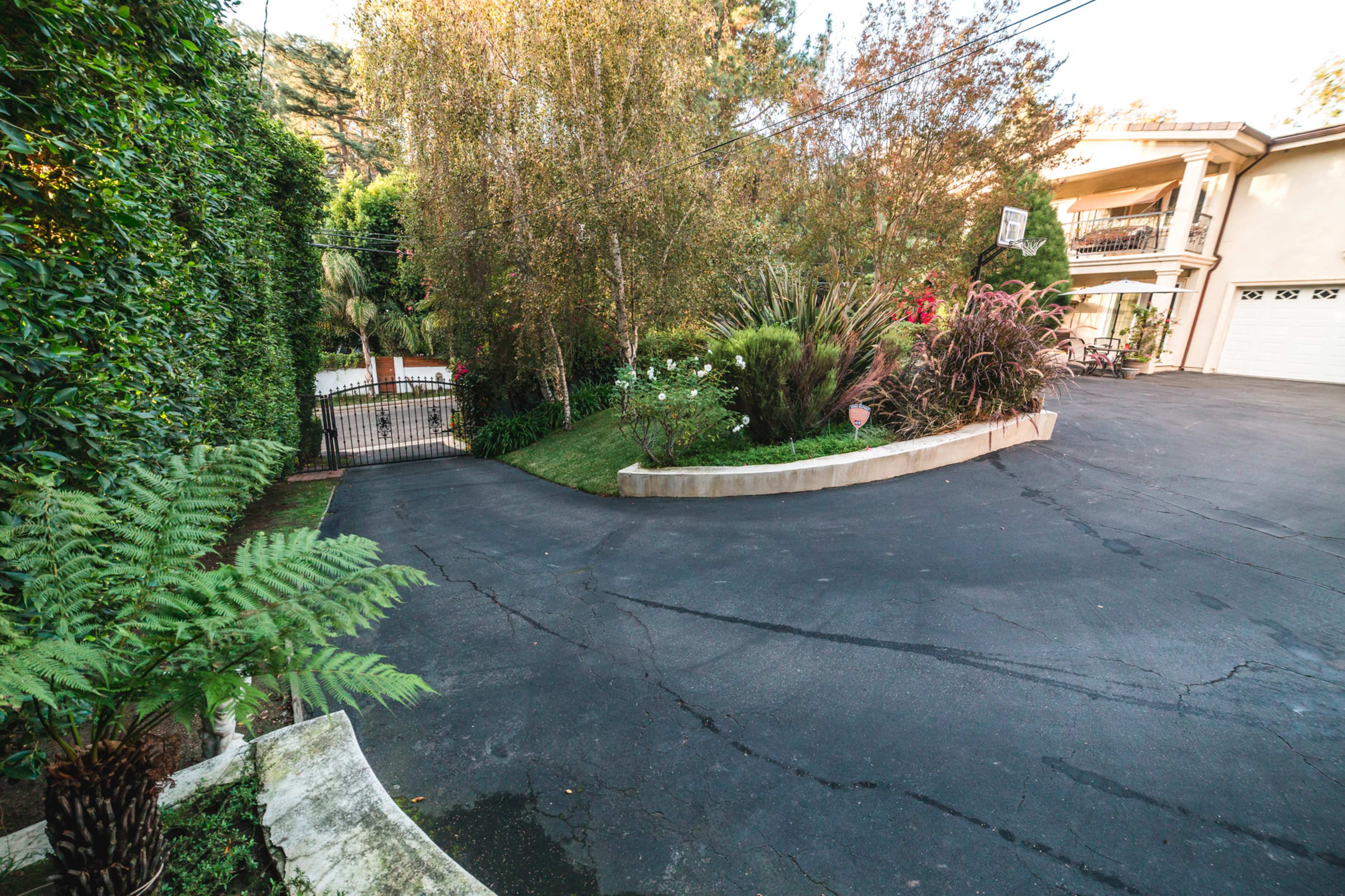 The image shows a curved driveway leading to a gated entrance surrounded by greenery and landscaping.