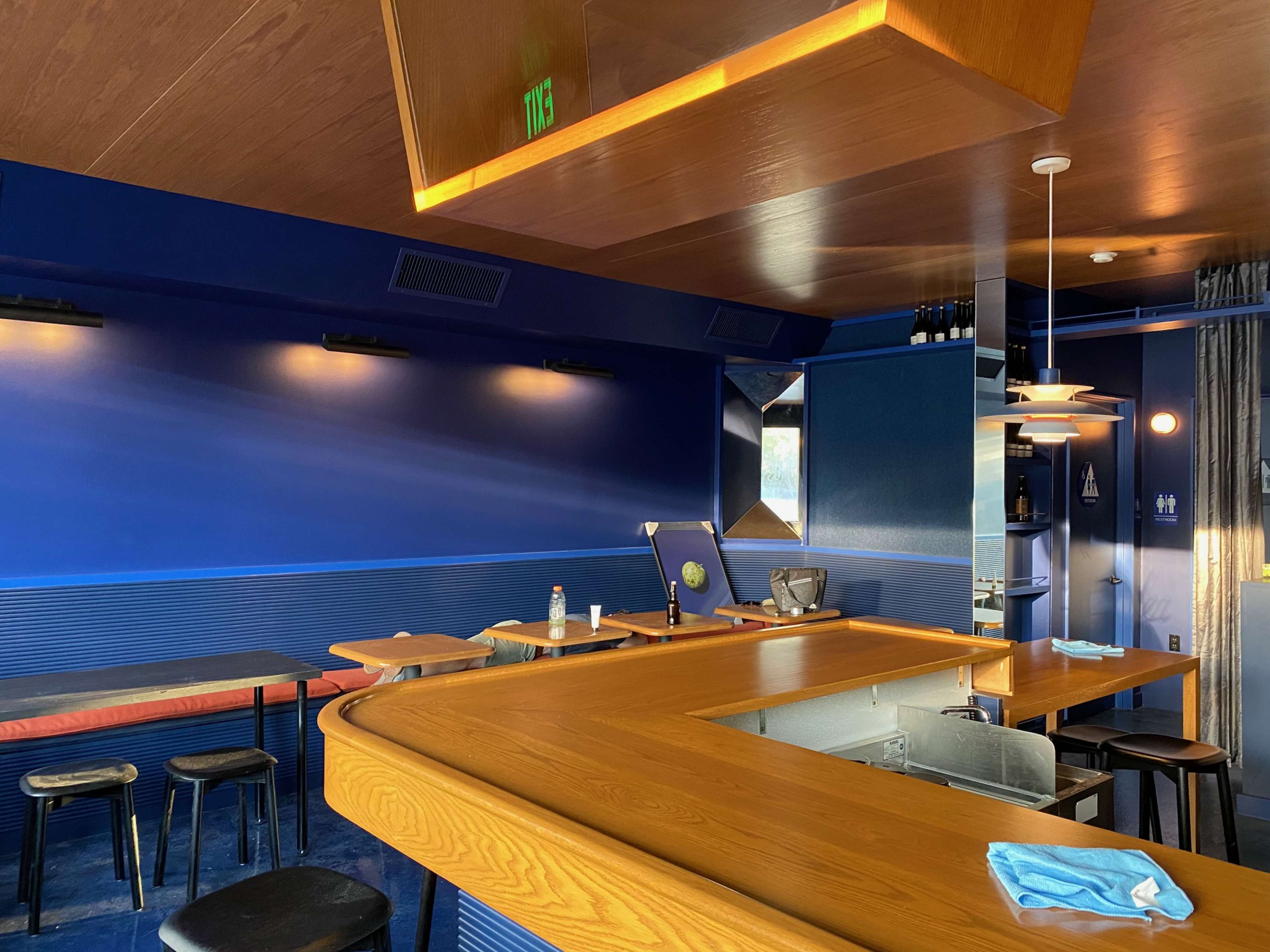 A modern bar area with a curved wooden counter, blue walls, and a few tables and stools.