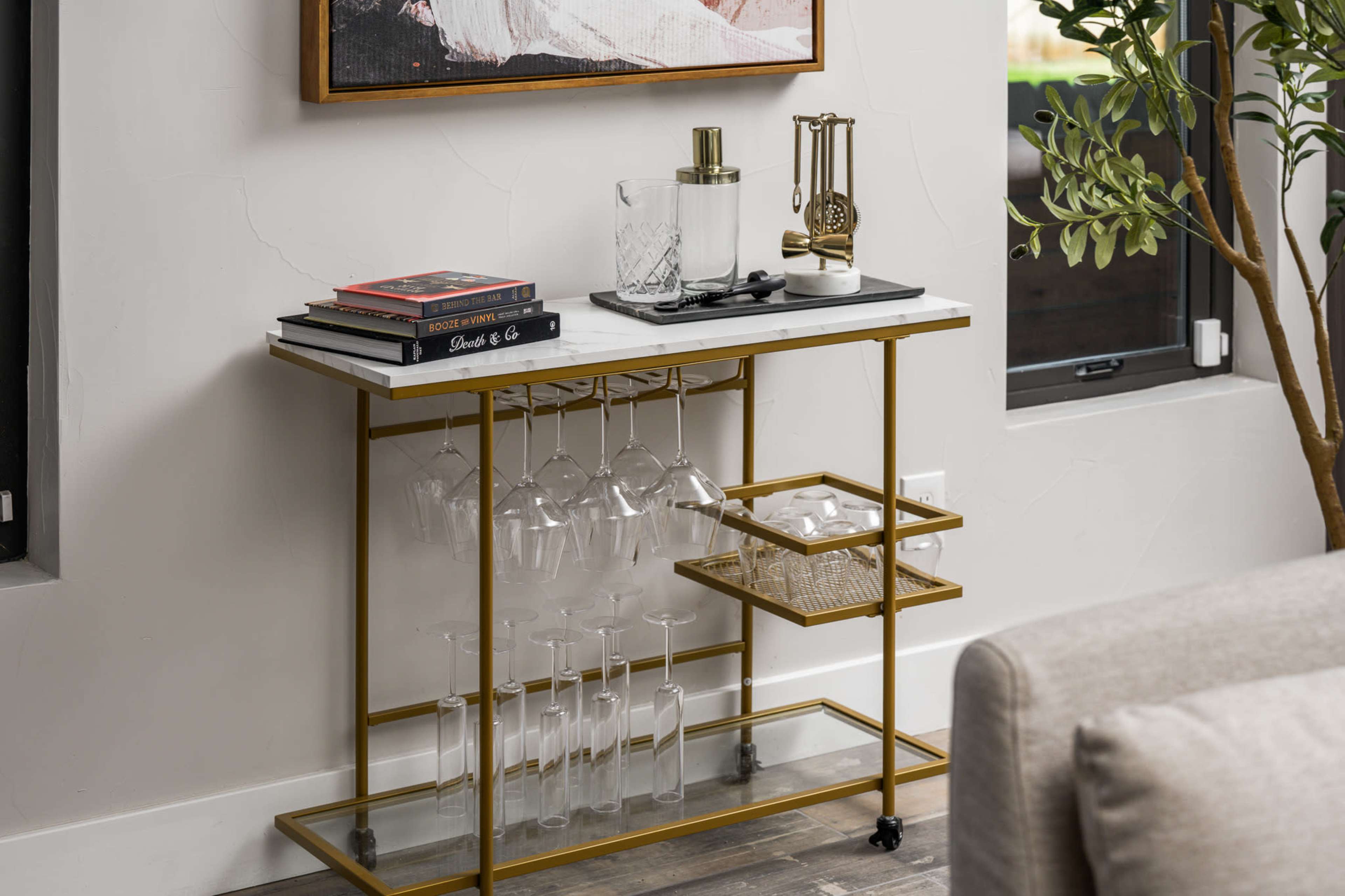 A bar cart features glassware hanging below and shelves above, adorned with a decanter and books.