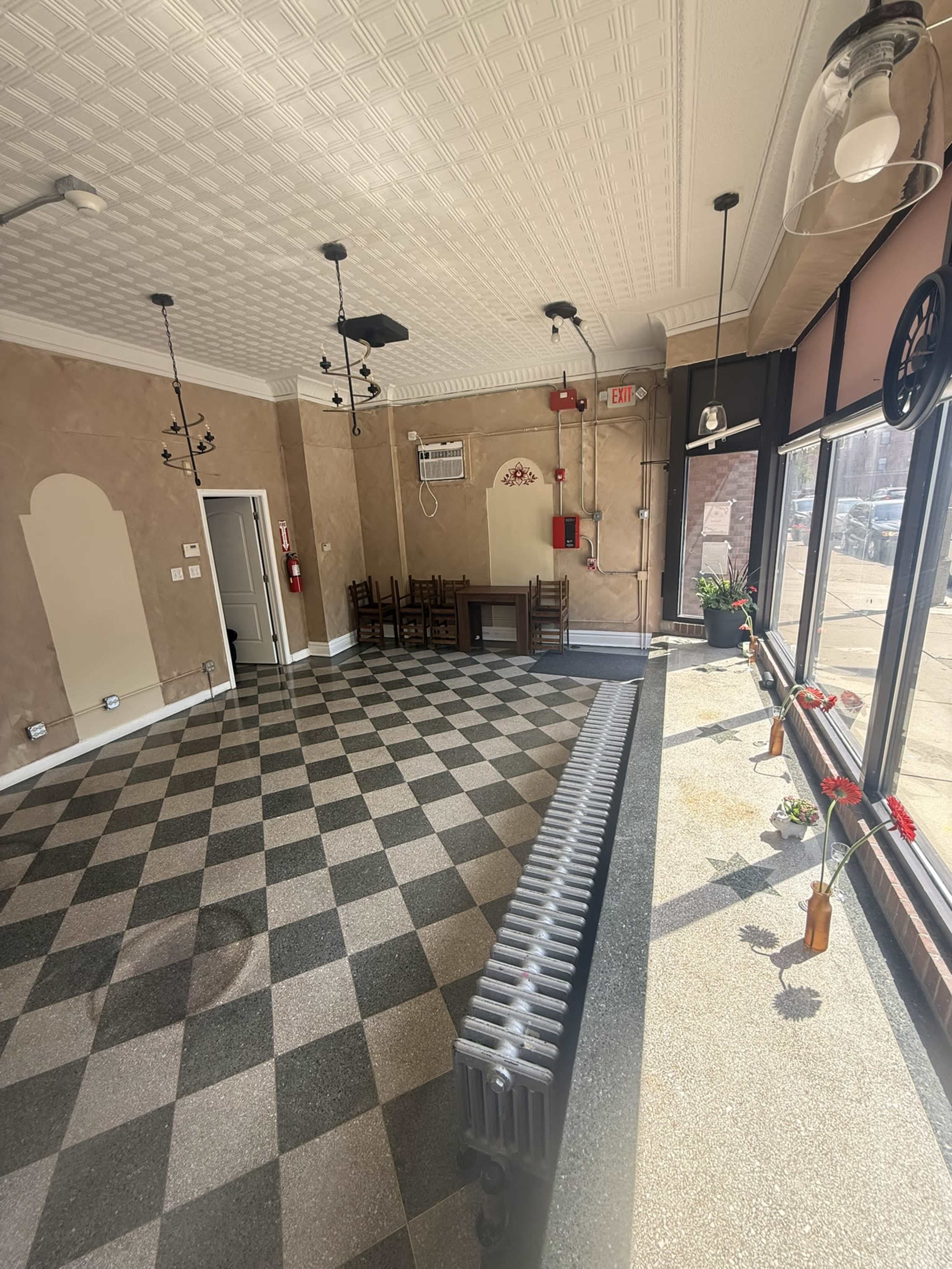 The image shows the interior of an empty room with checkered flooring, decorative wall features, and various fixtures like light fixtures and a radiator.