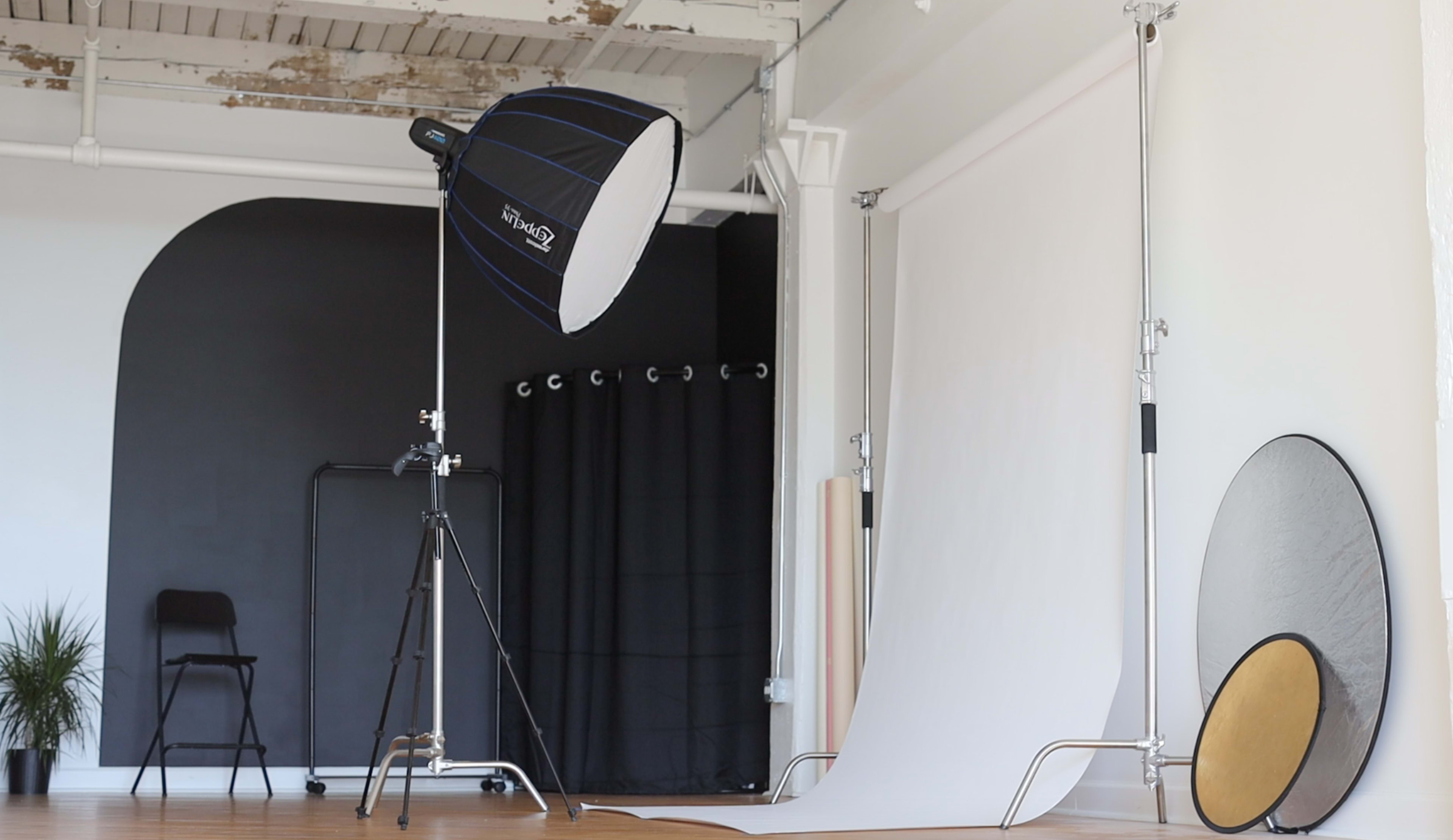 A photography studio with a light source on a stand, a seamless backdrop, and various studio equipment arranged neatly.