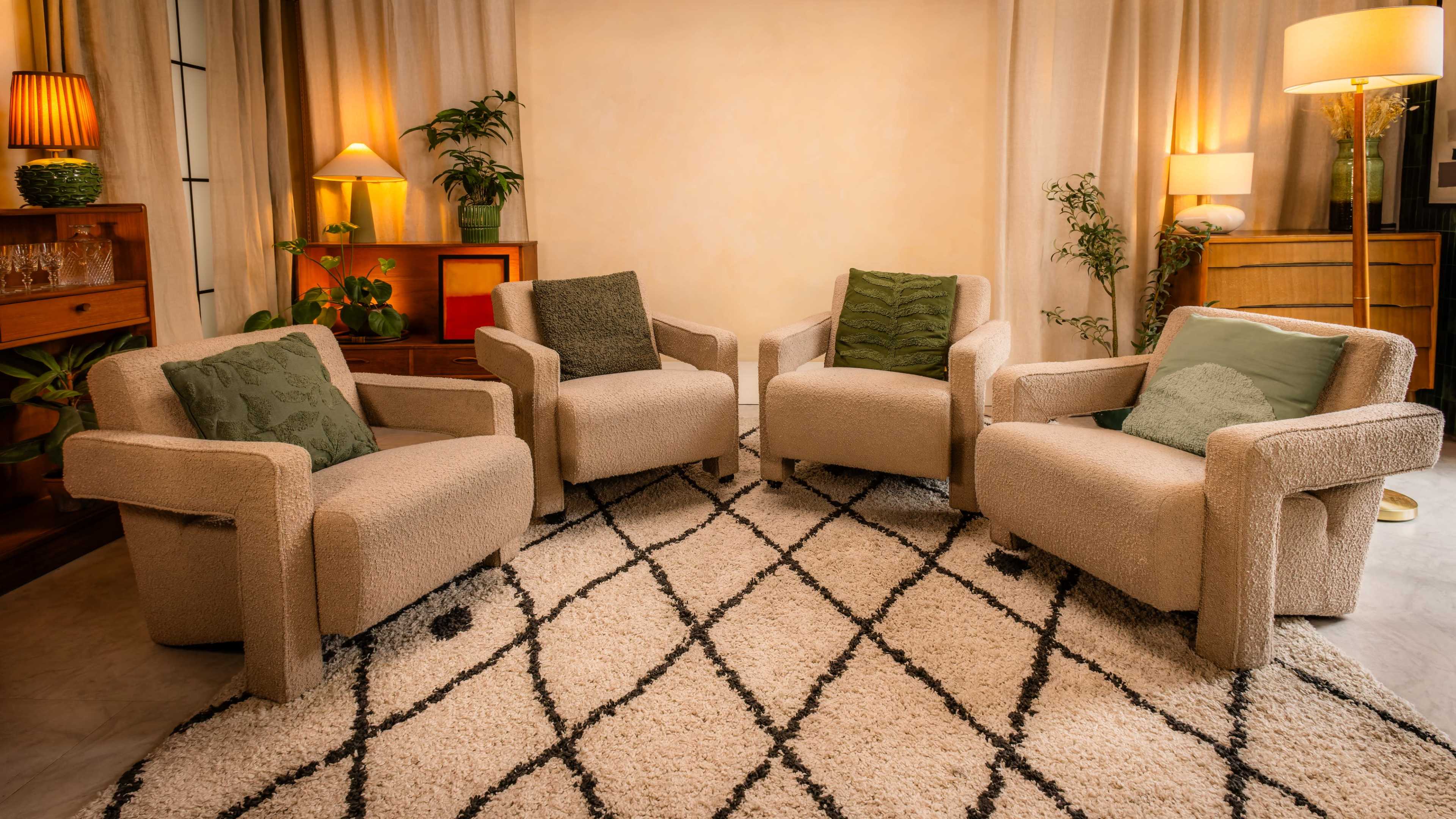 The image shows four beige armchairs with green decorative pillows arranged around a patterned rug in a warmly lit living space.