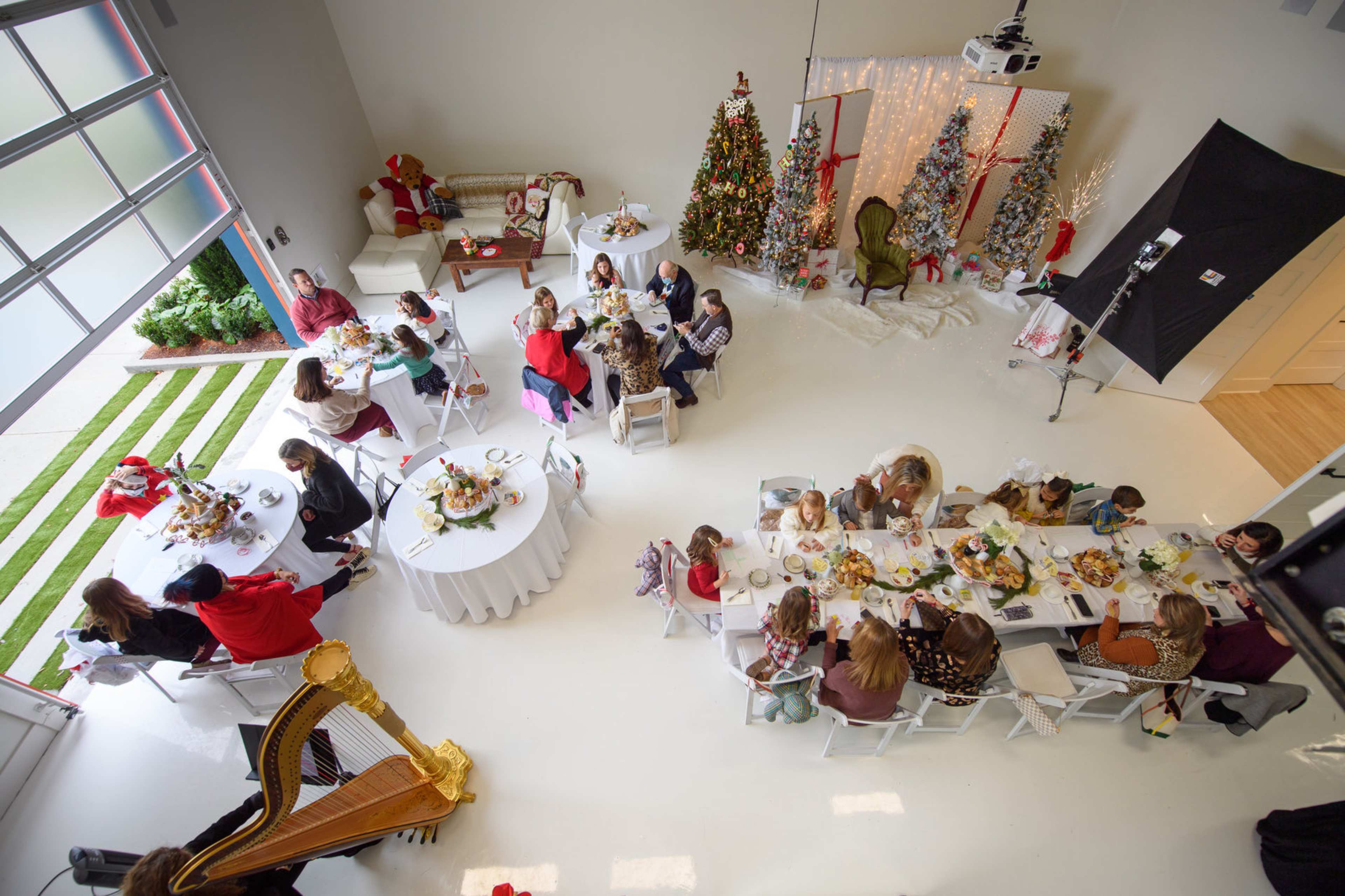 A large gathering of people is seated around tables in a spacious room decorated with Christmas trees and festive decor.