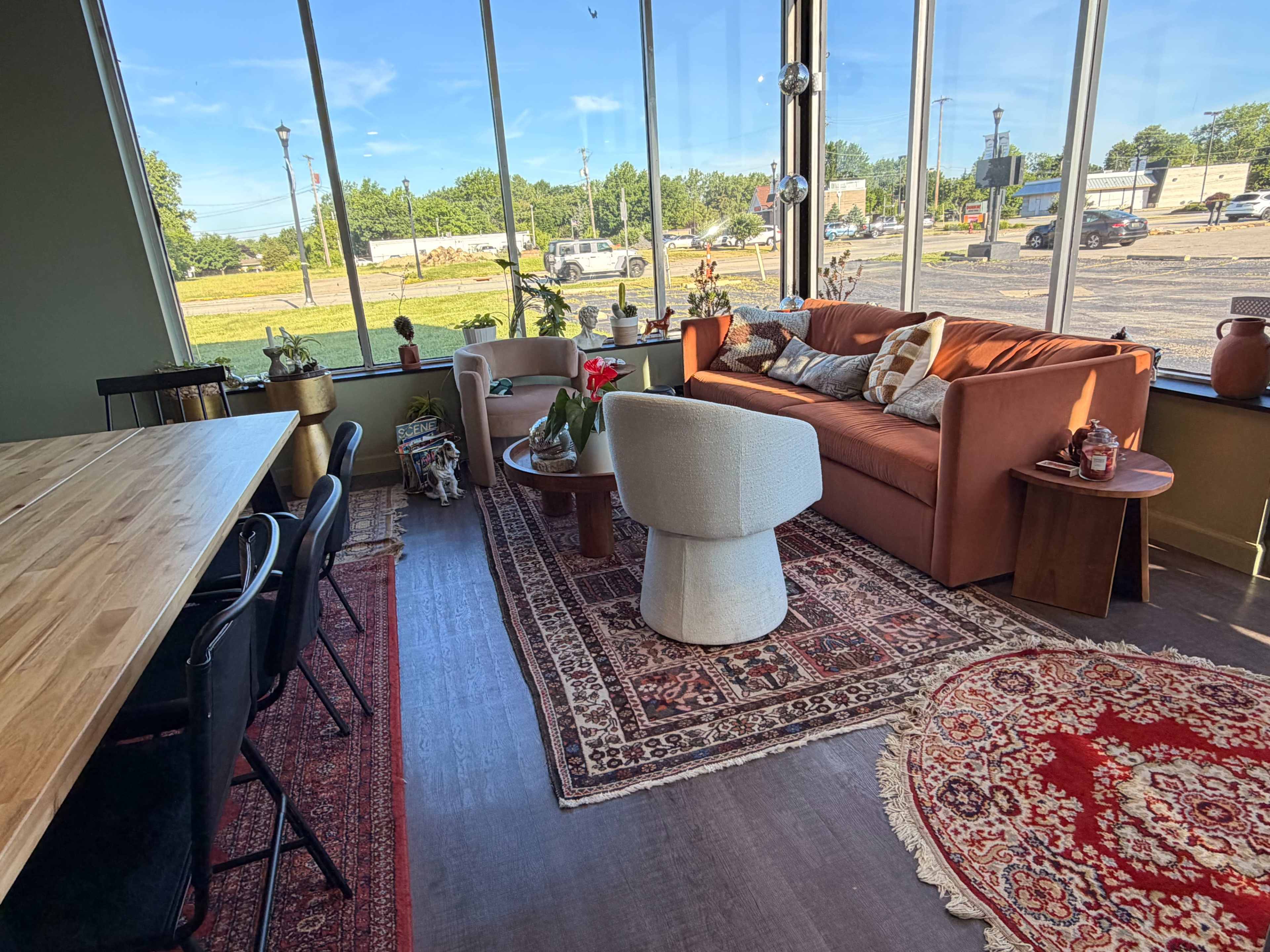 The image shows a modern interior space featuring a cozy seating area with a sofa, decorative rugs, and a dining table with chairs by large windows.