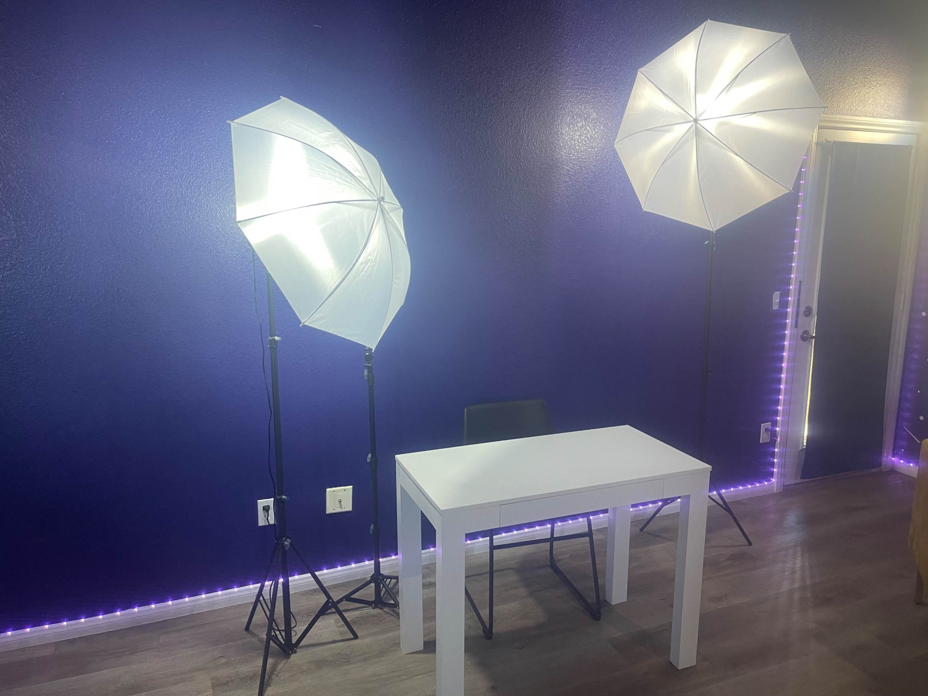 A brightly lit room with two softbox lights positioned on either side of a white table against a purple wall.