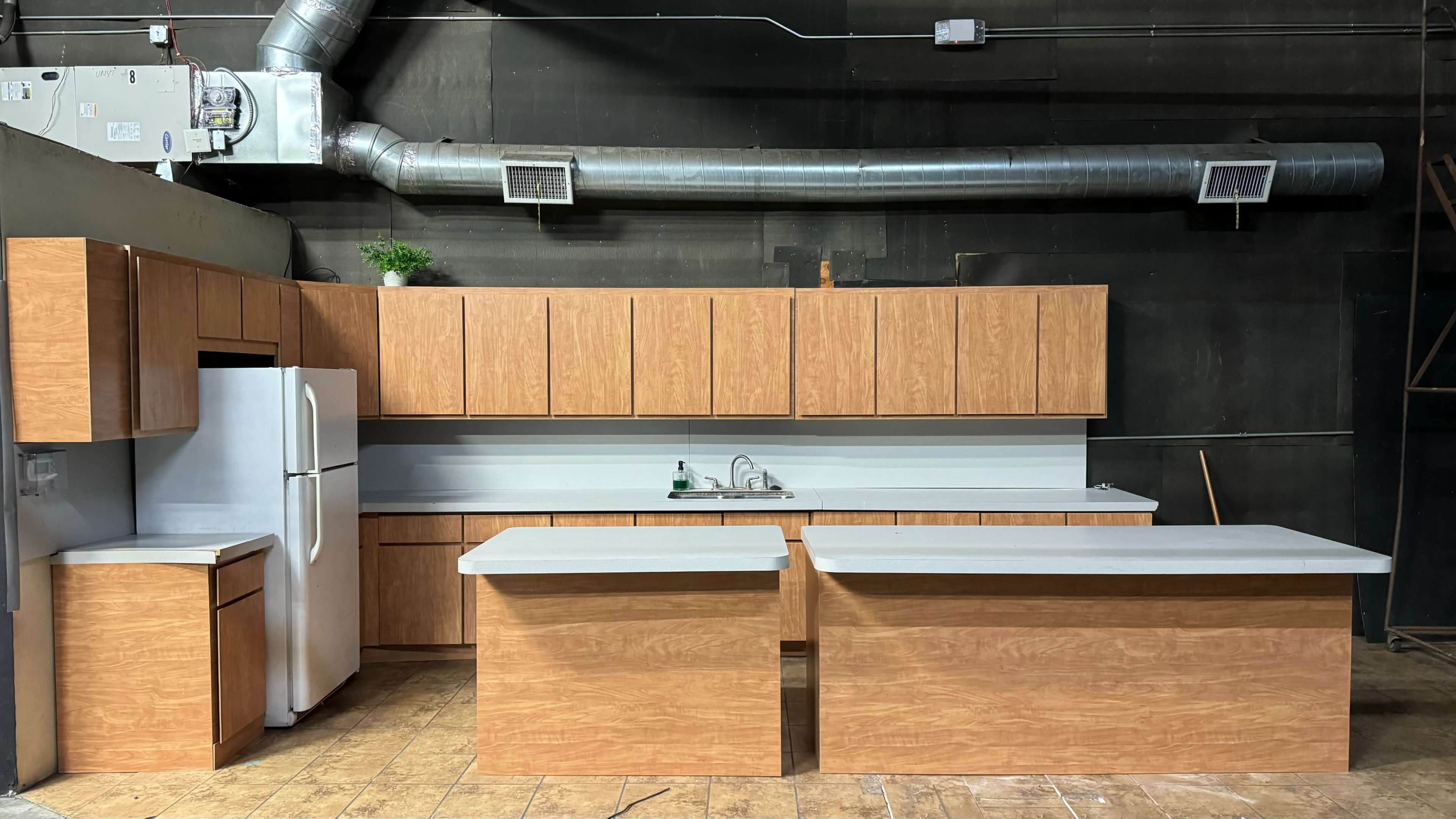 The image shows a modern kitchen display featuring wooden cabinetry, a white refrigerator, and a central island with a gray countertop.