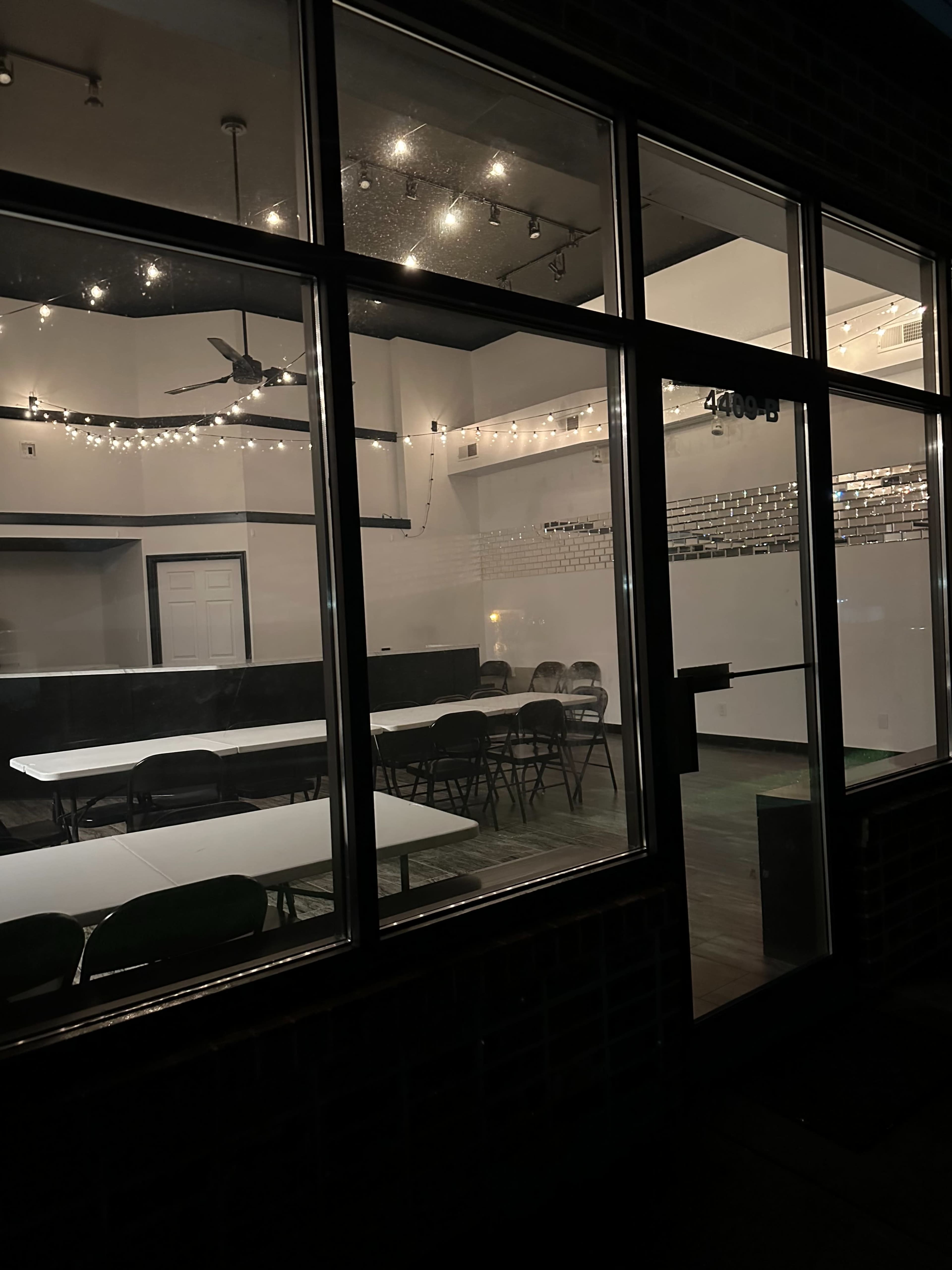 The image shows a dimly lit interior of a venue featuring several tables and chairs arranged for an event.