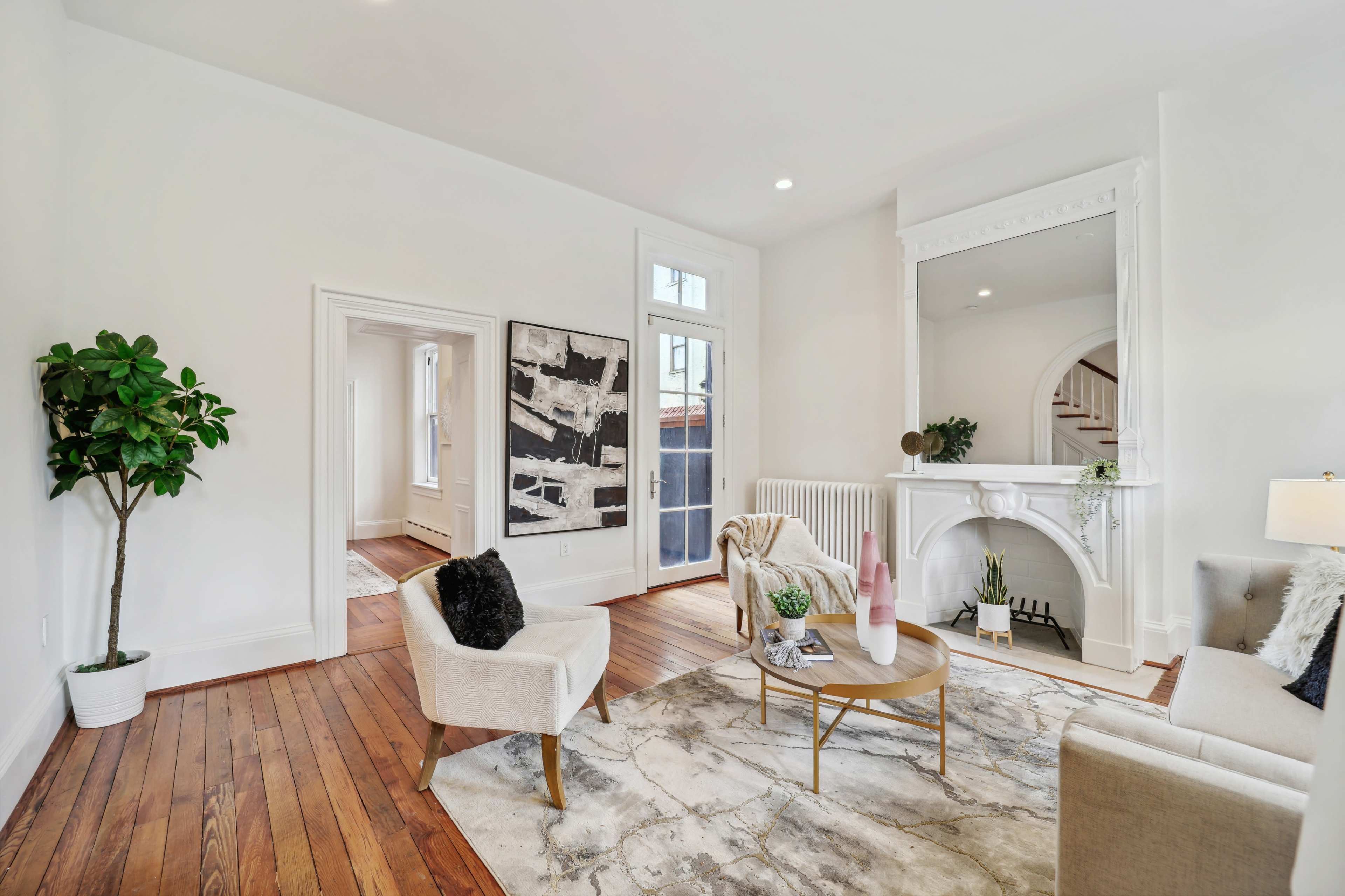 A bright, open living room featuring a round coffee table, two chairs, a decorative rug, and a white marble fireplace.
