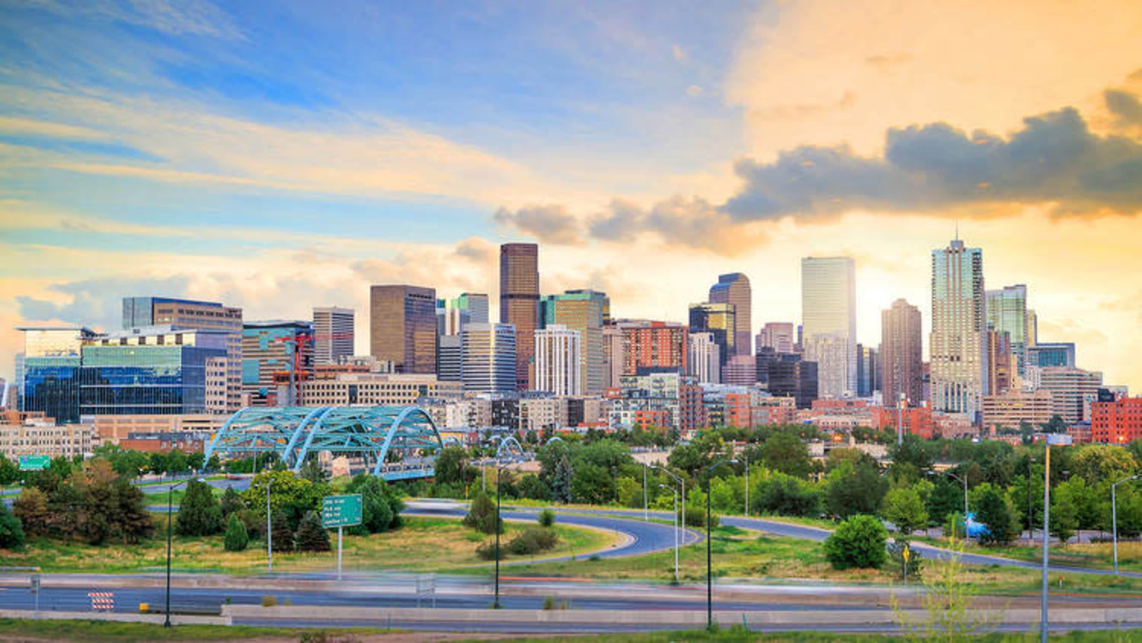 A city skyline featuring tall buildings and green spaces under a colorful sky.