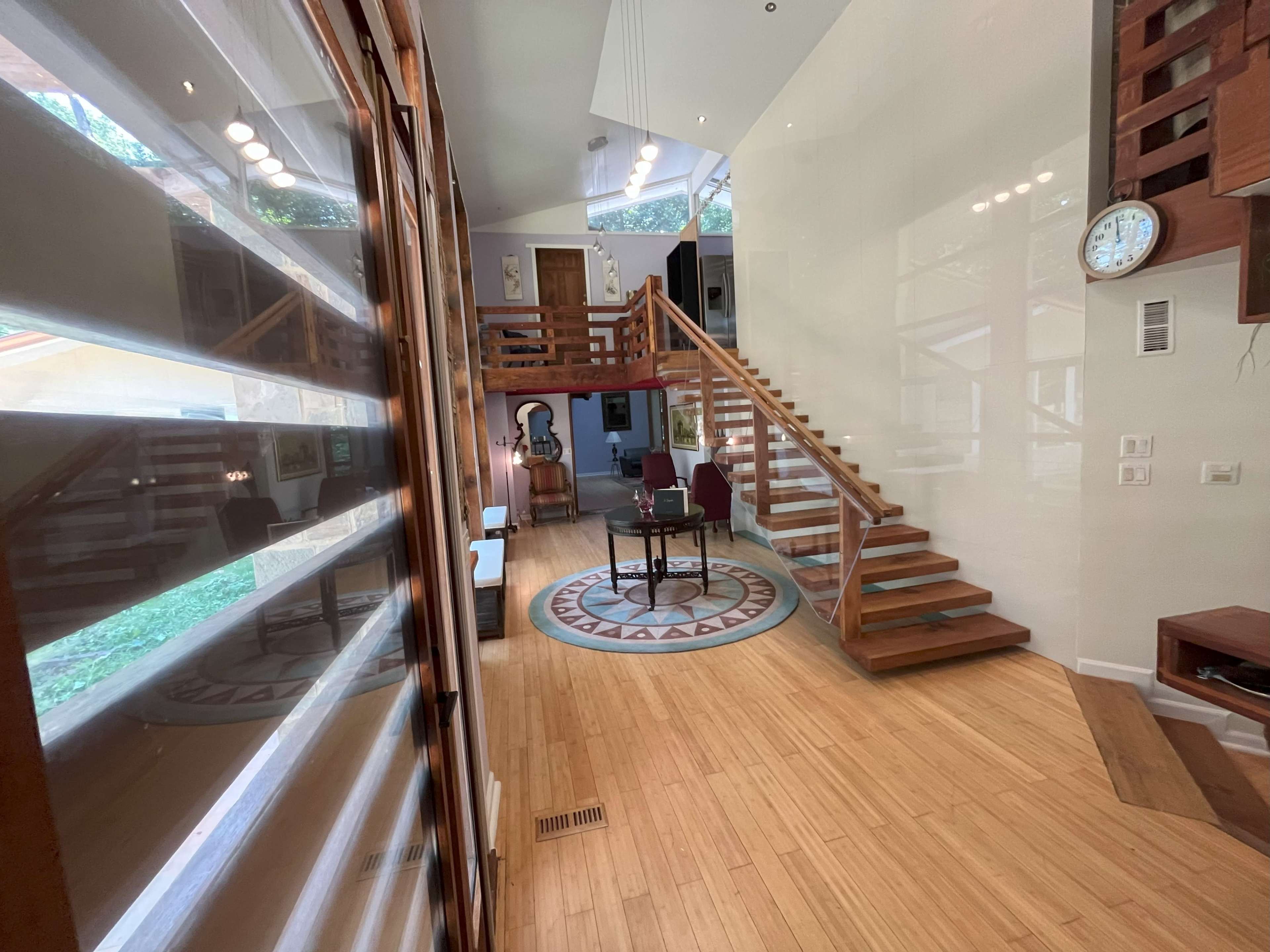 A spacious, modern entryway with wooden stairs leading to an upper level and a round rug set in the center.