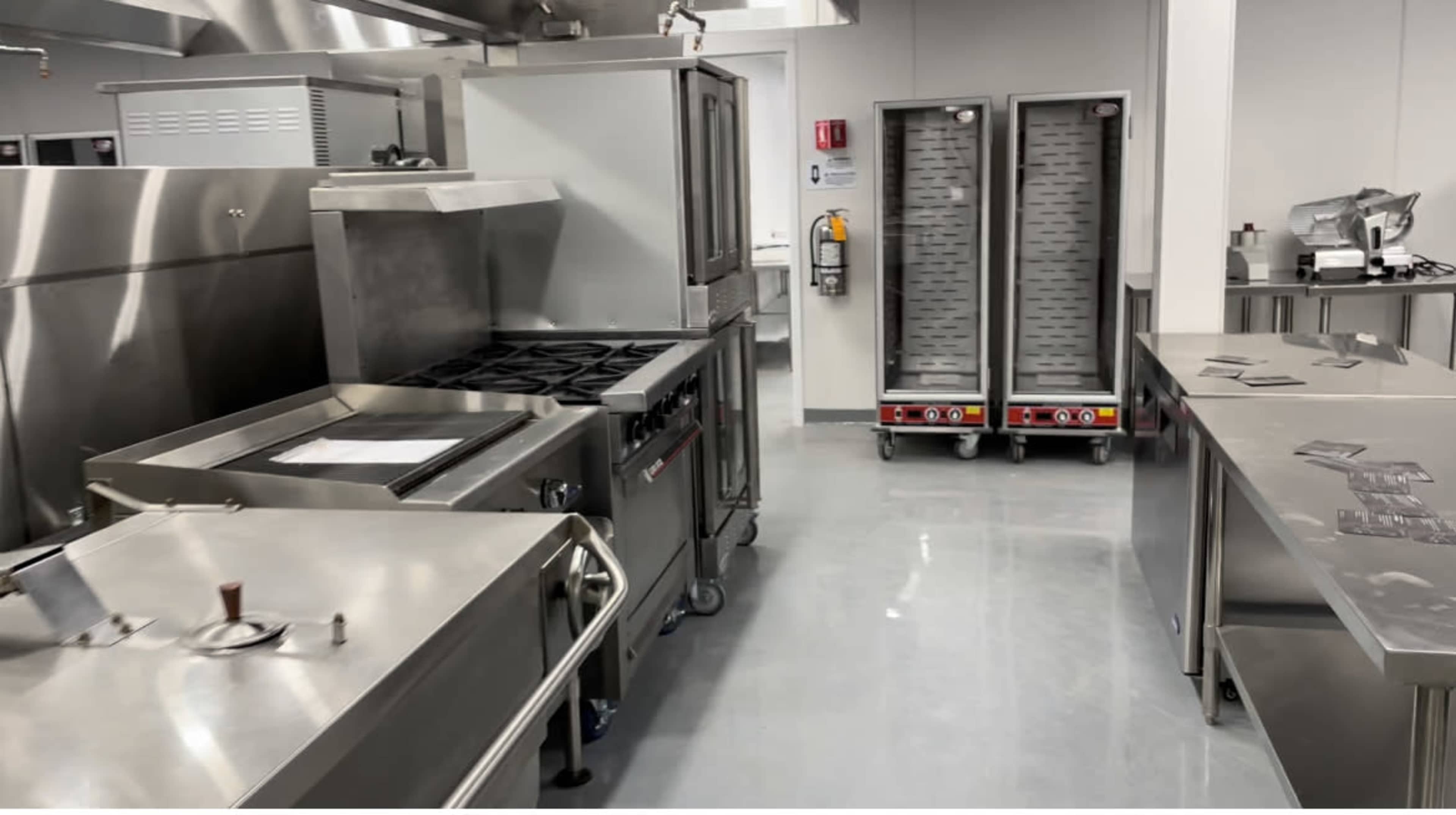 A modern commercial kitchen equipped with stainless steel appliances, cooking stations, and food transport carts.