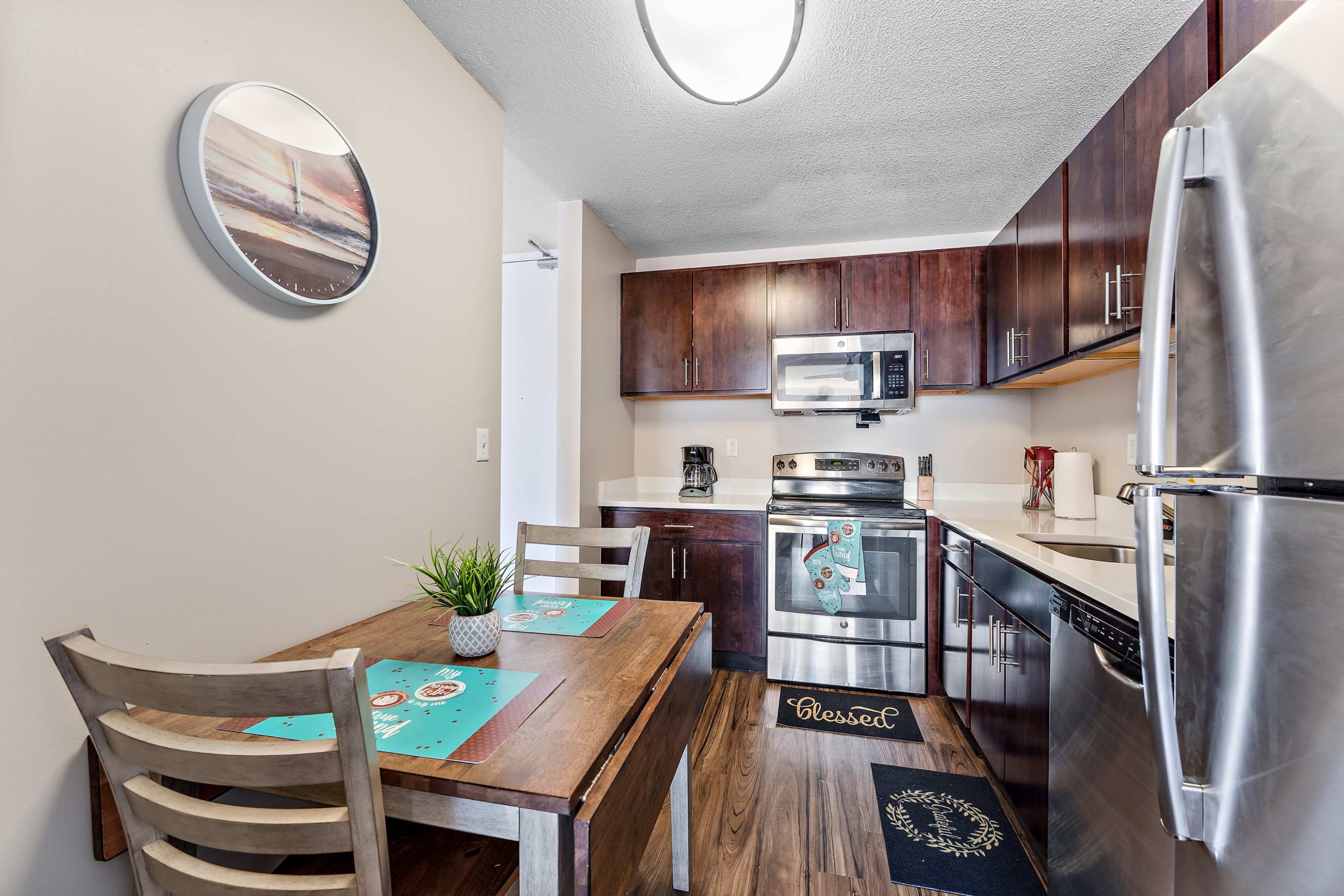 A modern kitchen with dark wood cabinetry, stainless steel appliances, and a small dining table set for two.