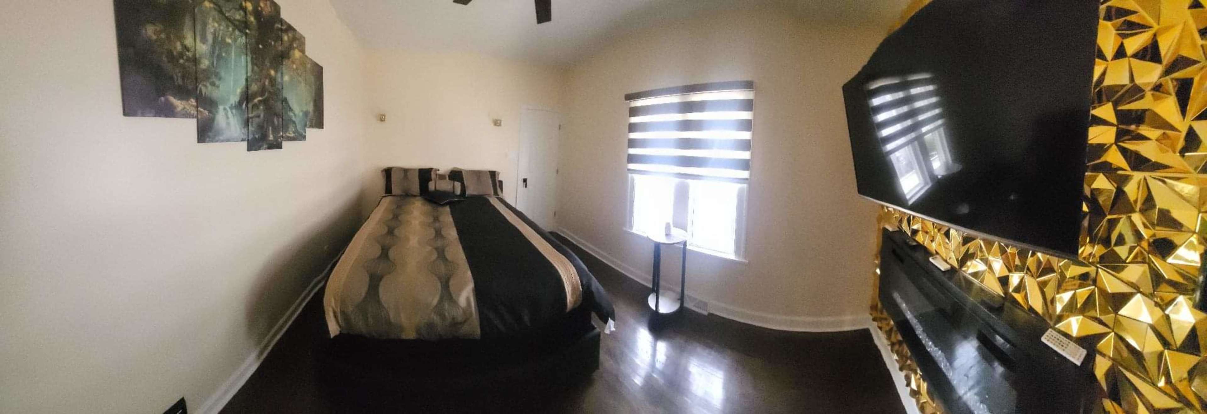 The image shows a well-decorated bedroom featuring a bed with dark bedding, a striped window shade, and a decorative wall with a golden geometric design.
