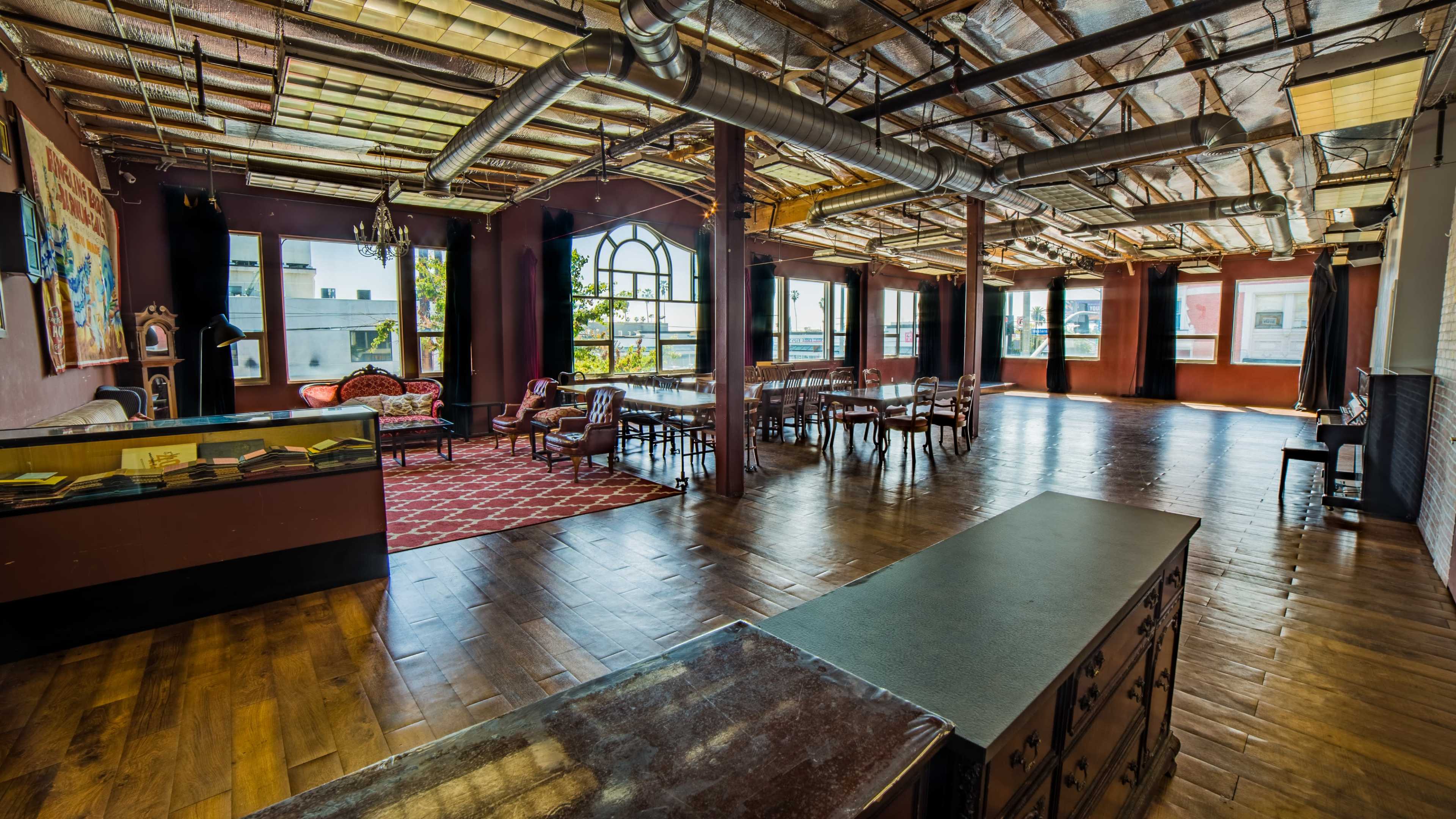 A spacious, well-lit room with a mix of seating areas, including a couch and dining tables, and large windows providing natural light.