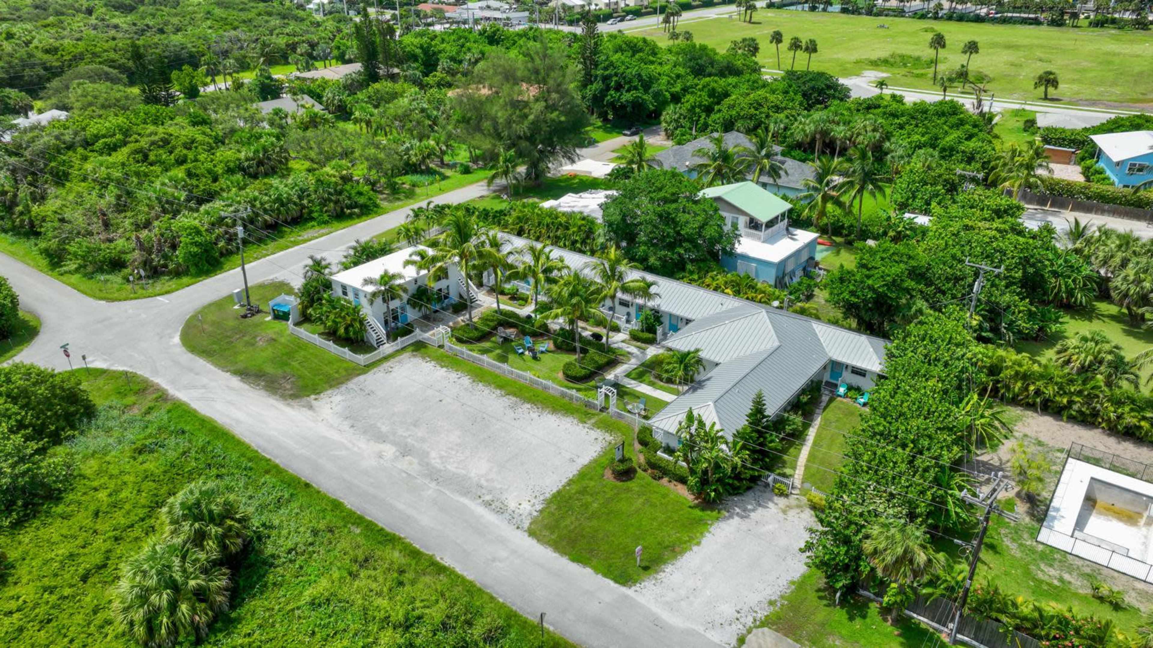 The image shows an aerial view of a property with several buildings surrounded by greenery and well-maintained landscaping near a road.