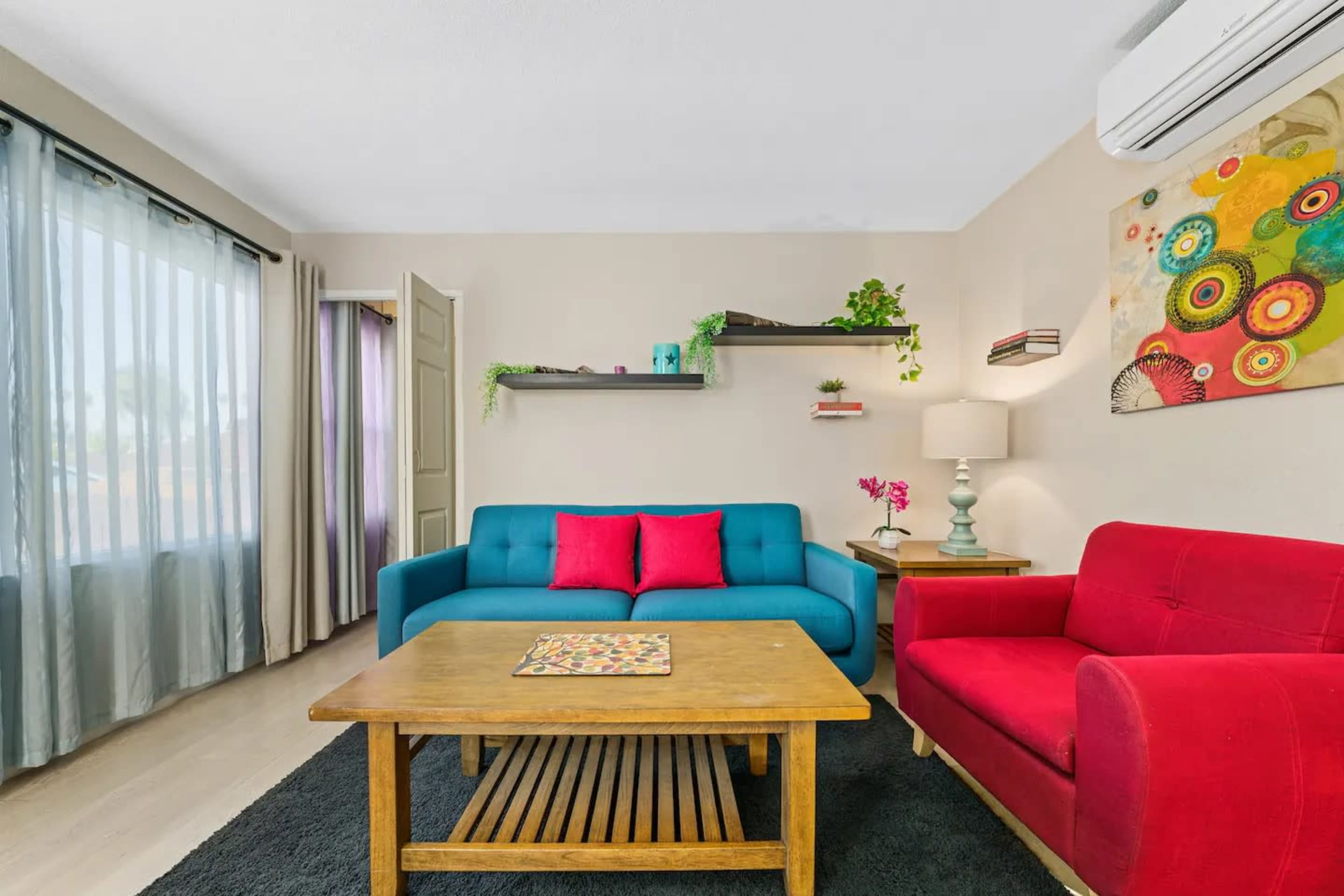 The image shows a living room with a blue couch, a red armchair, a wooden coffee table, and decorative shelves on the wall.