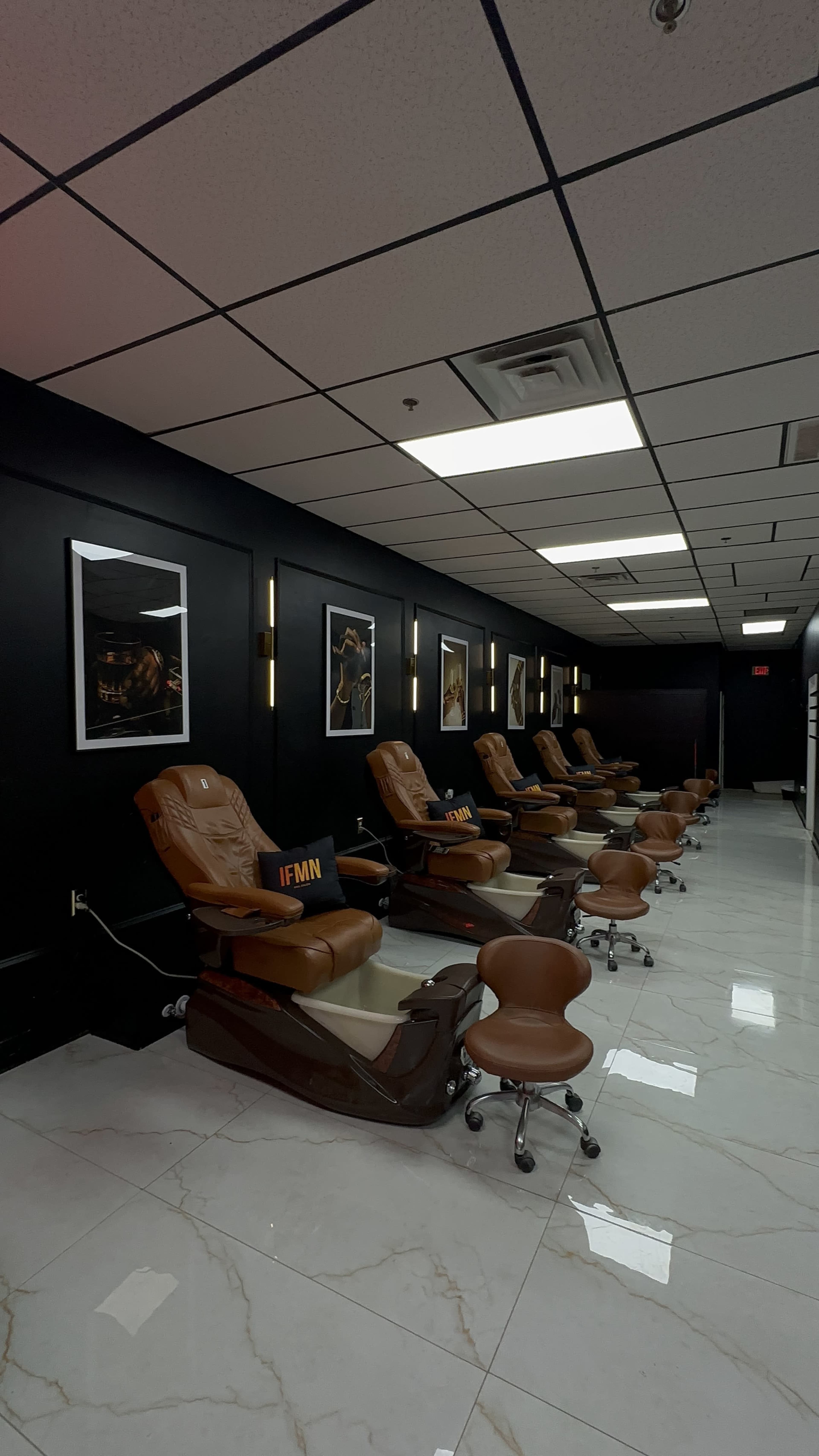 The image shows a nail salon interior featuring pedicure chairs arranged in a row against a black wall adorned with framed artwork.