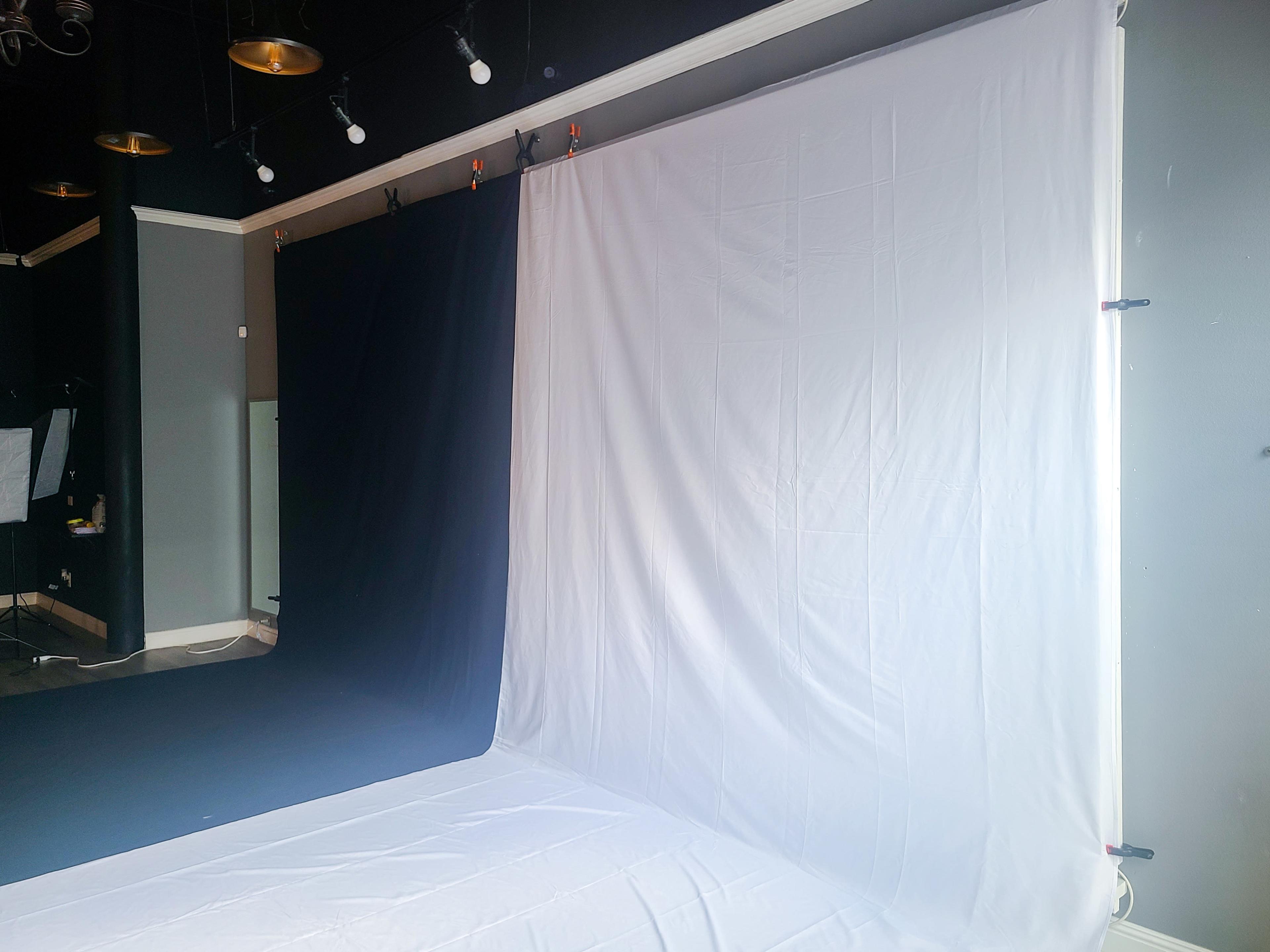 A photography studio with a white backdrop on the right and a black backdrop on the left, both hanging from the ceiling.