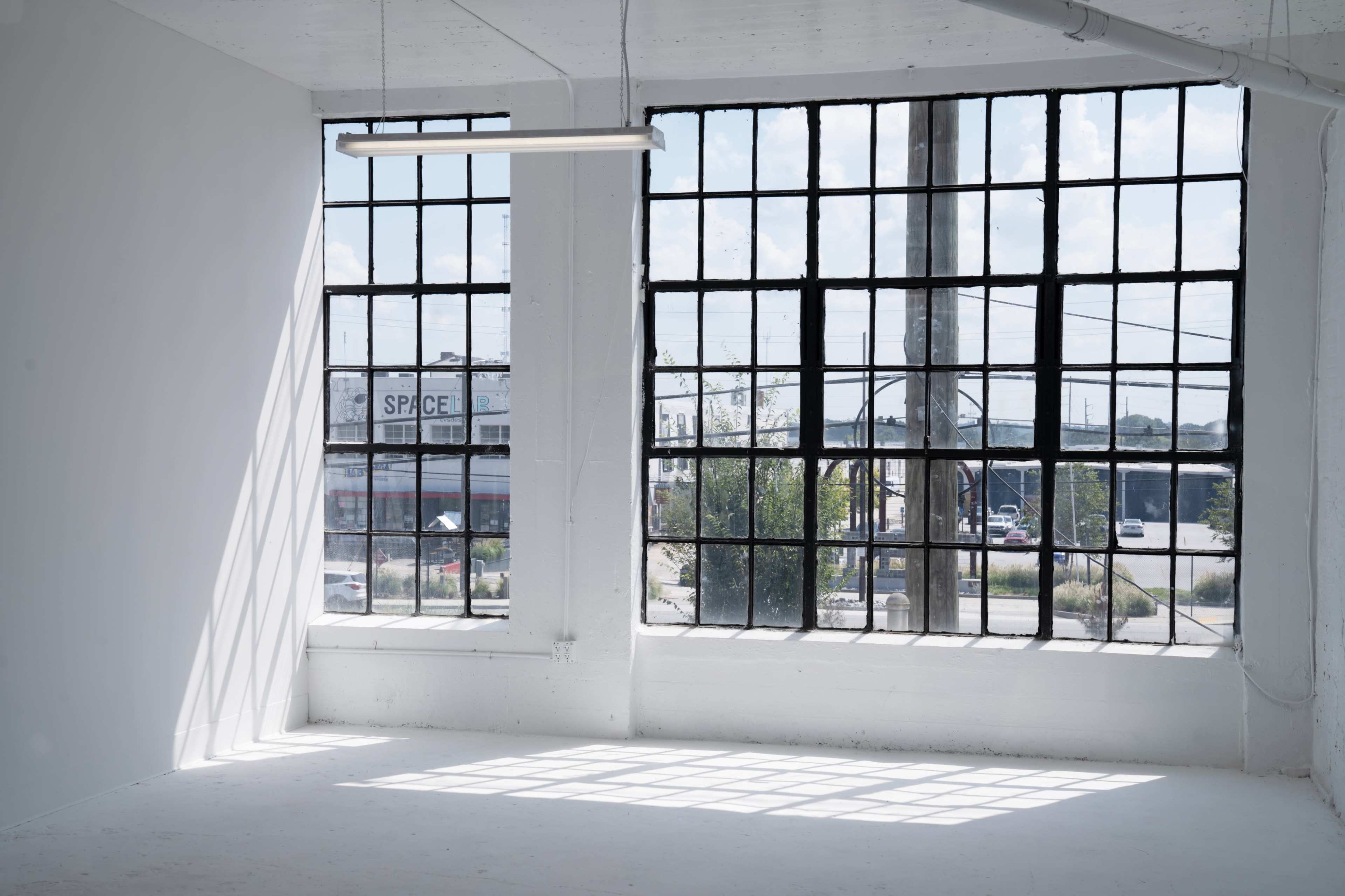 A bright, minimalist interior with large industrial windows overlooking a street area.