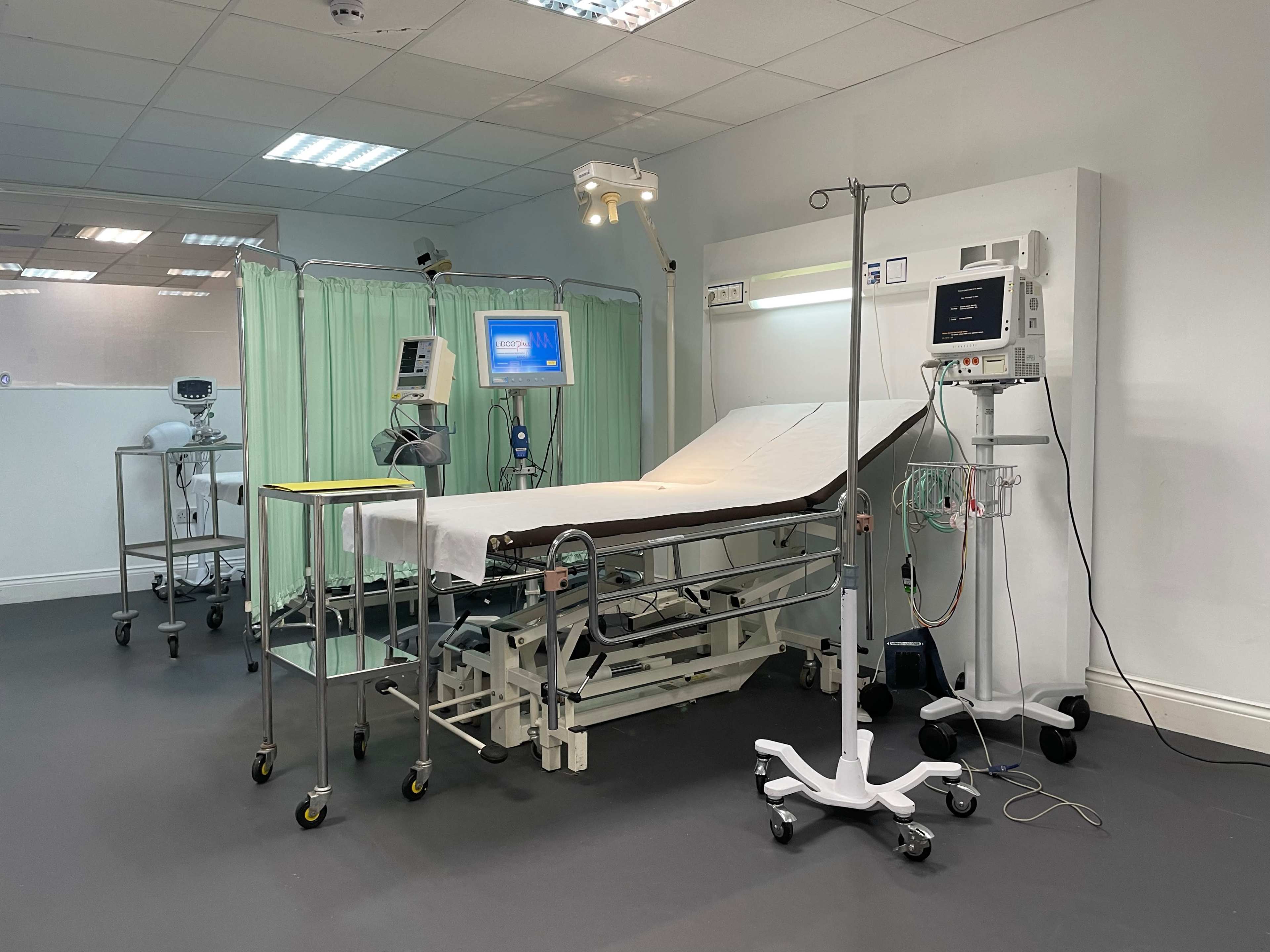 A medical examination room equipped with a hospital bed, medical monitors, and various medical equipment.