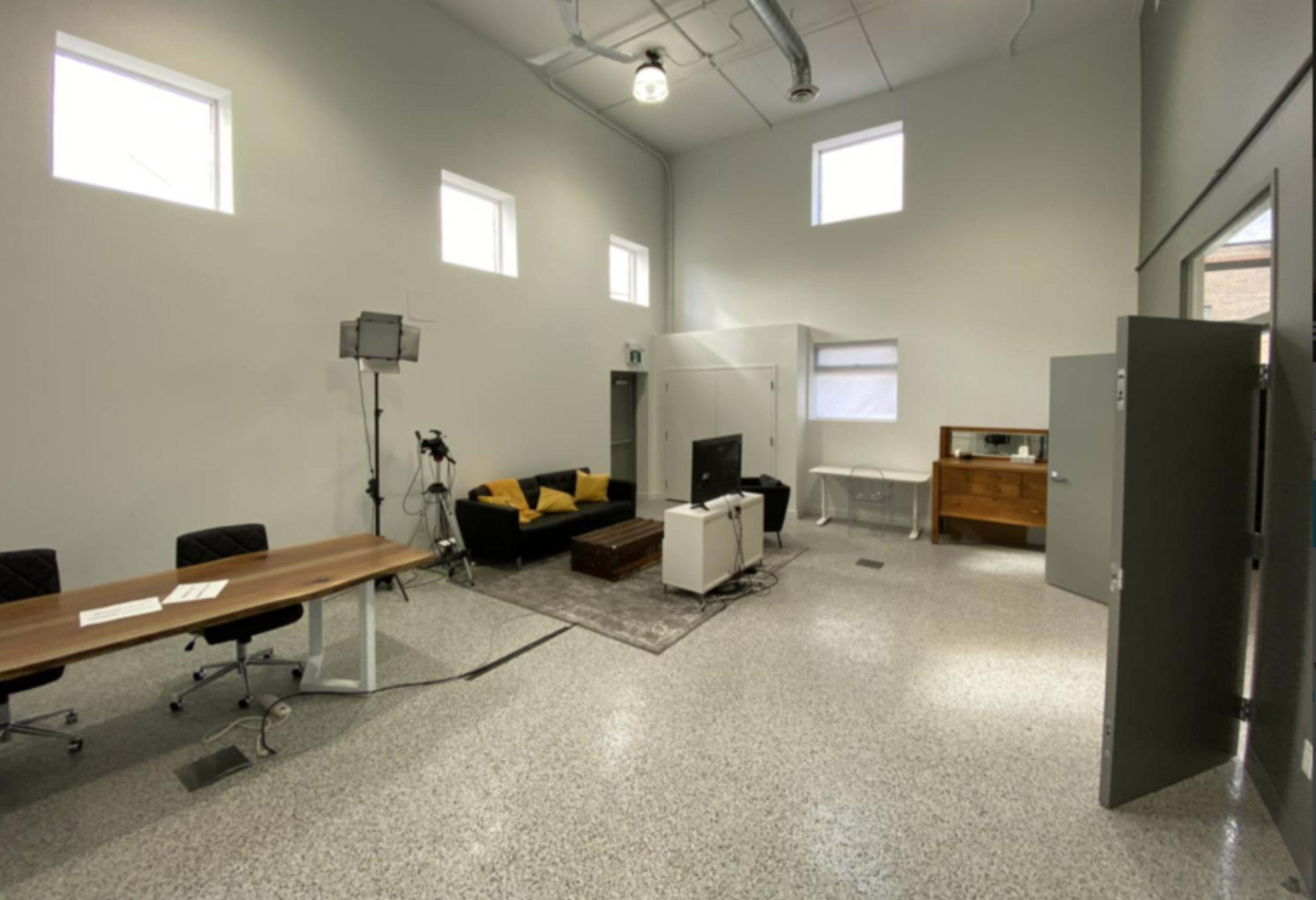 A spacious, minimalistic room featuring a couch, a television, a table with chairs, and a wooden cabinet.