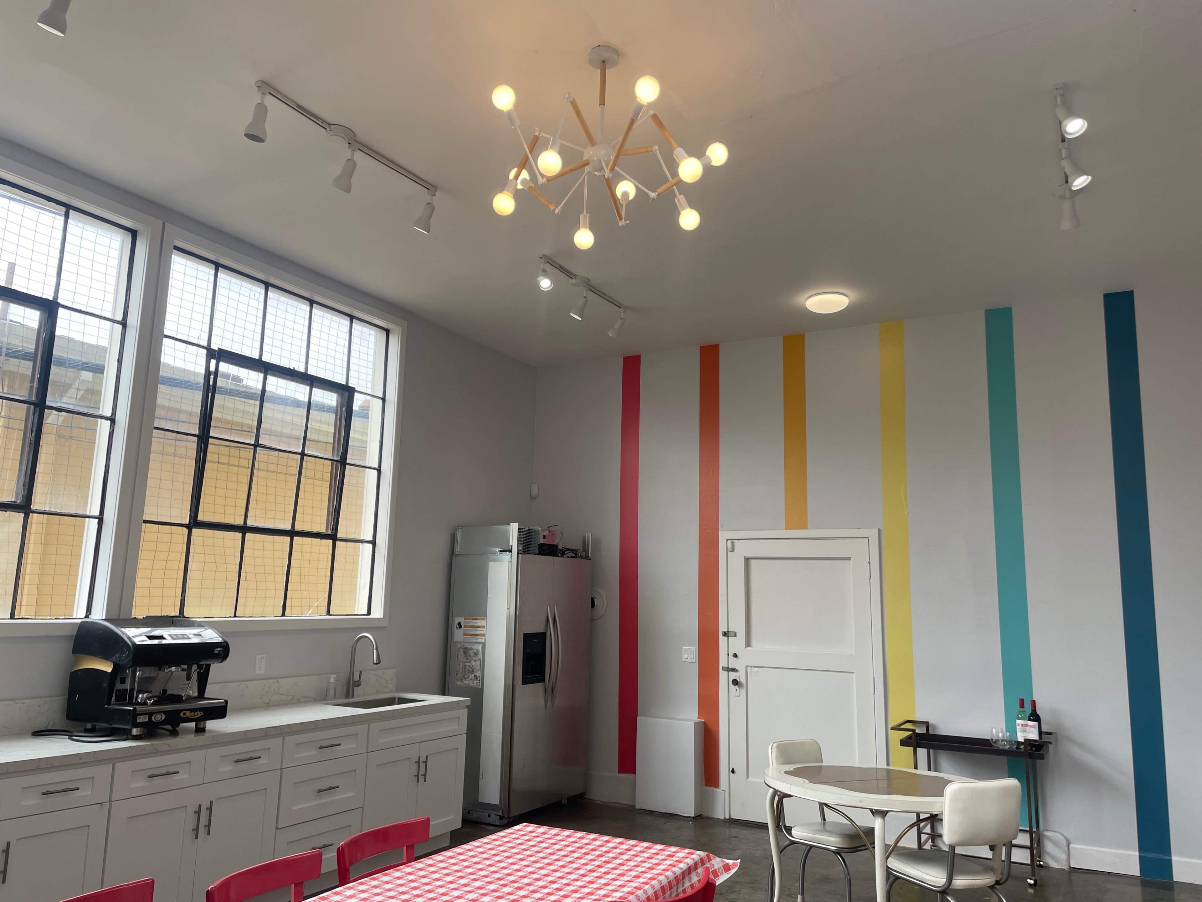 A bright kitchen features modern appliances, a checkered tablecloth-covered table, and colorful vertical stripes on the wall.