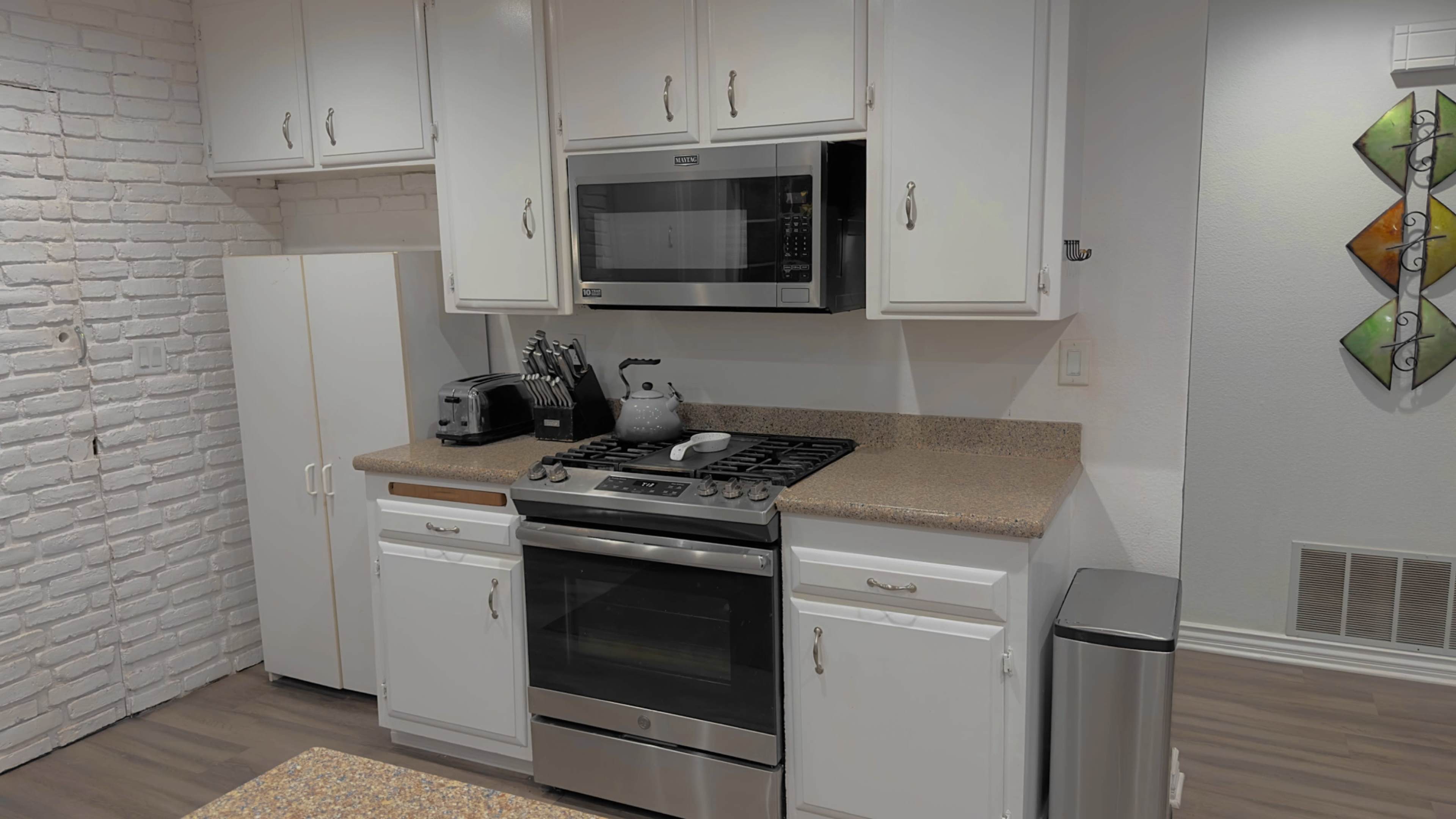 A kitchen with white cabinetry, a stainless steel microwave, a gas stove, and a light-colored countertop.
