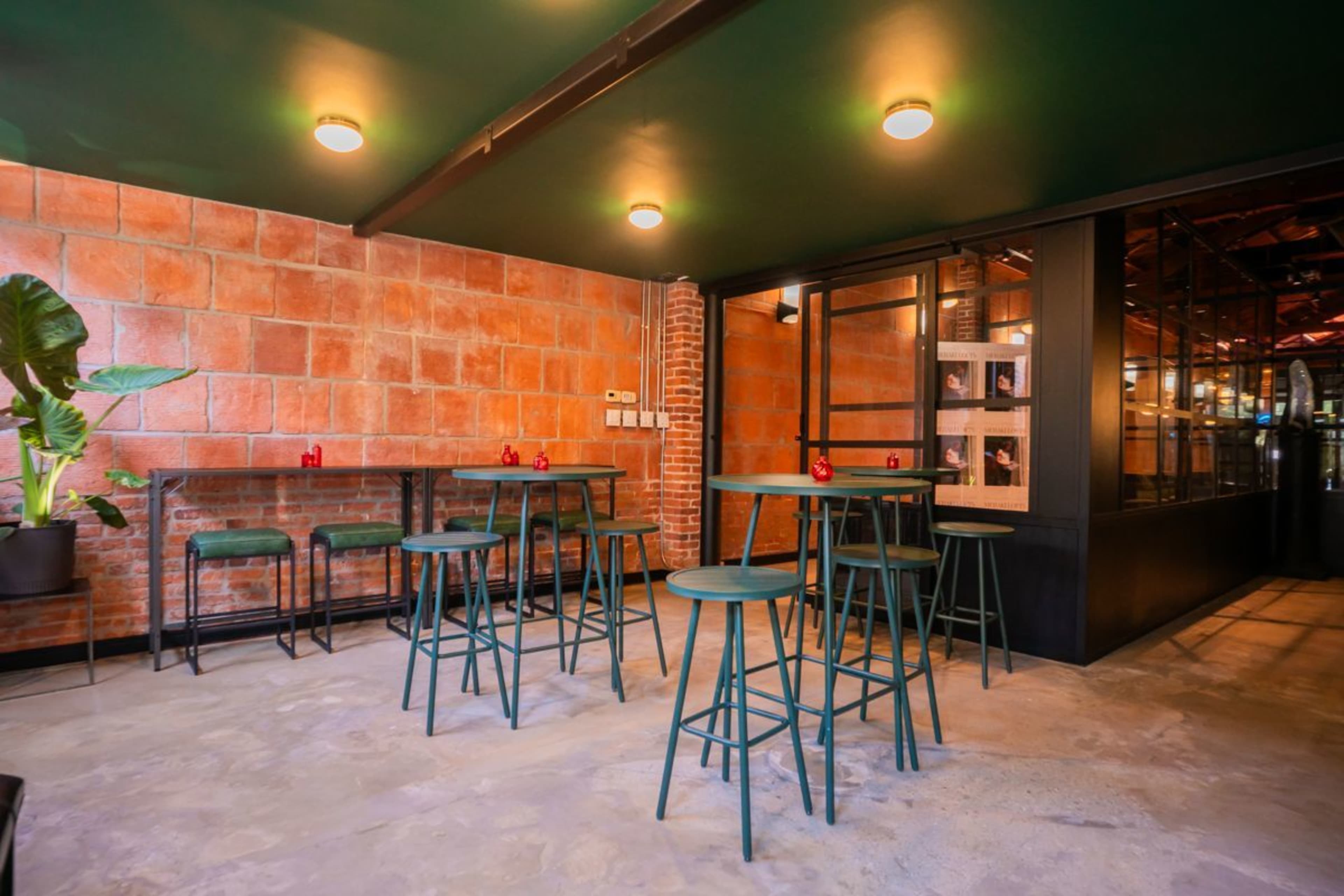 A modern interior features green bar stools and tables against a backdrop of exposed brick walls and polished concrete flooring.