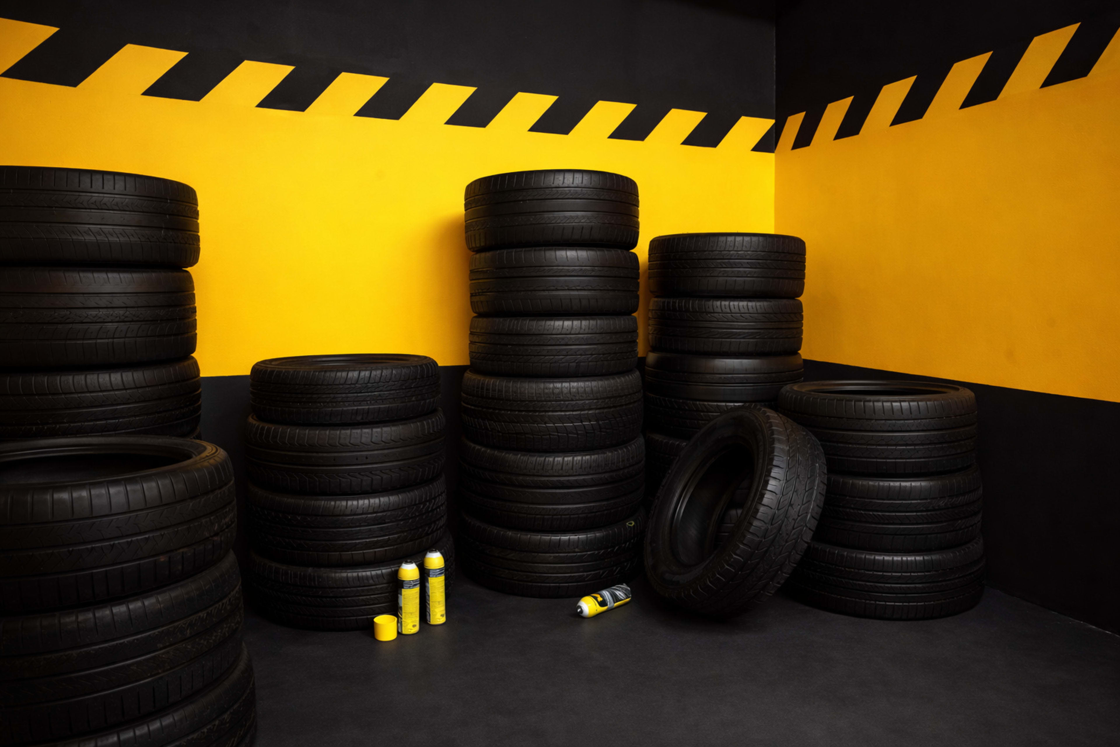 The image shows multiple stacks of black tires against a yellow and black wall in a garage-like setting.
