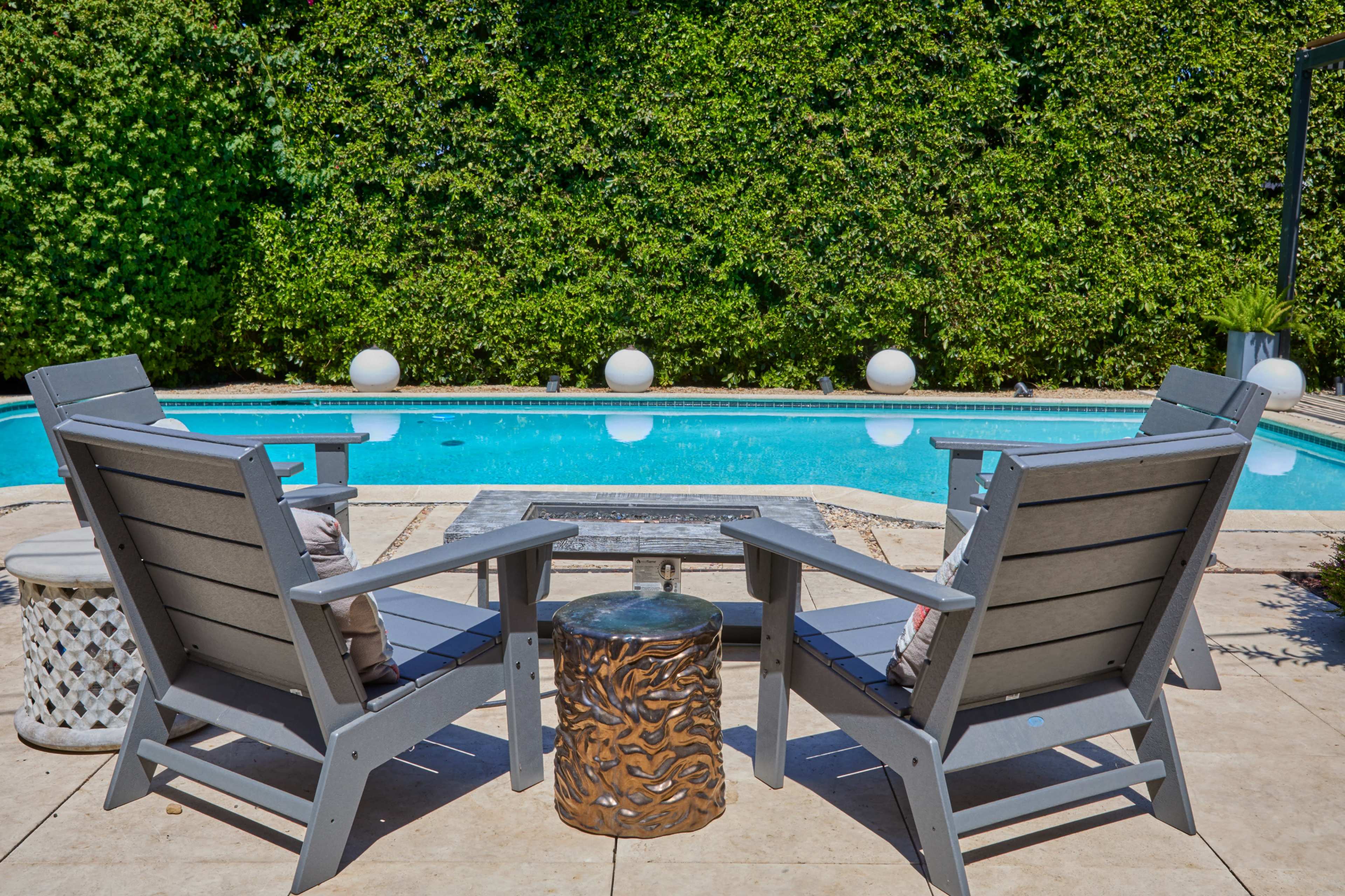 The image shows two gray Adirondack chairs facing a swimming pool, with a small decorative table between them.