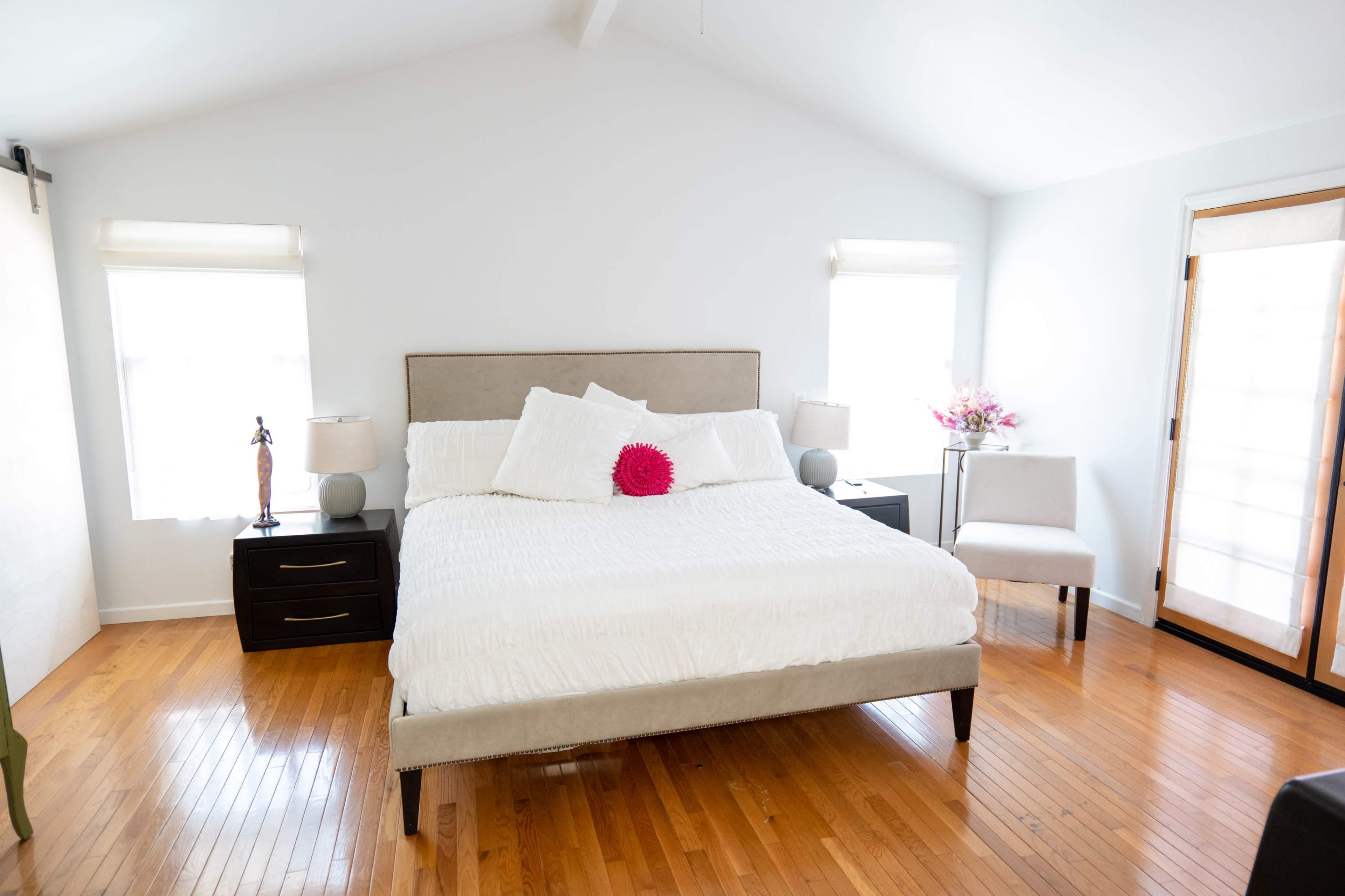 A neatly arranged bedroom features a large bed with white bedding, two bedside tables, and a chair near a window.