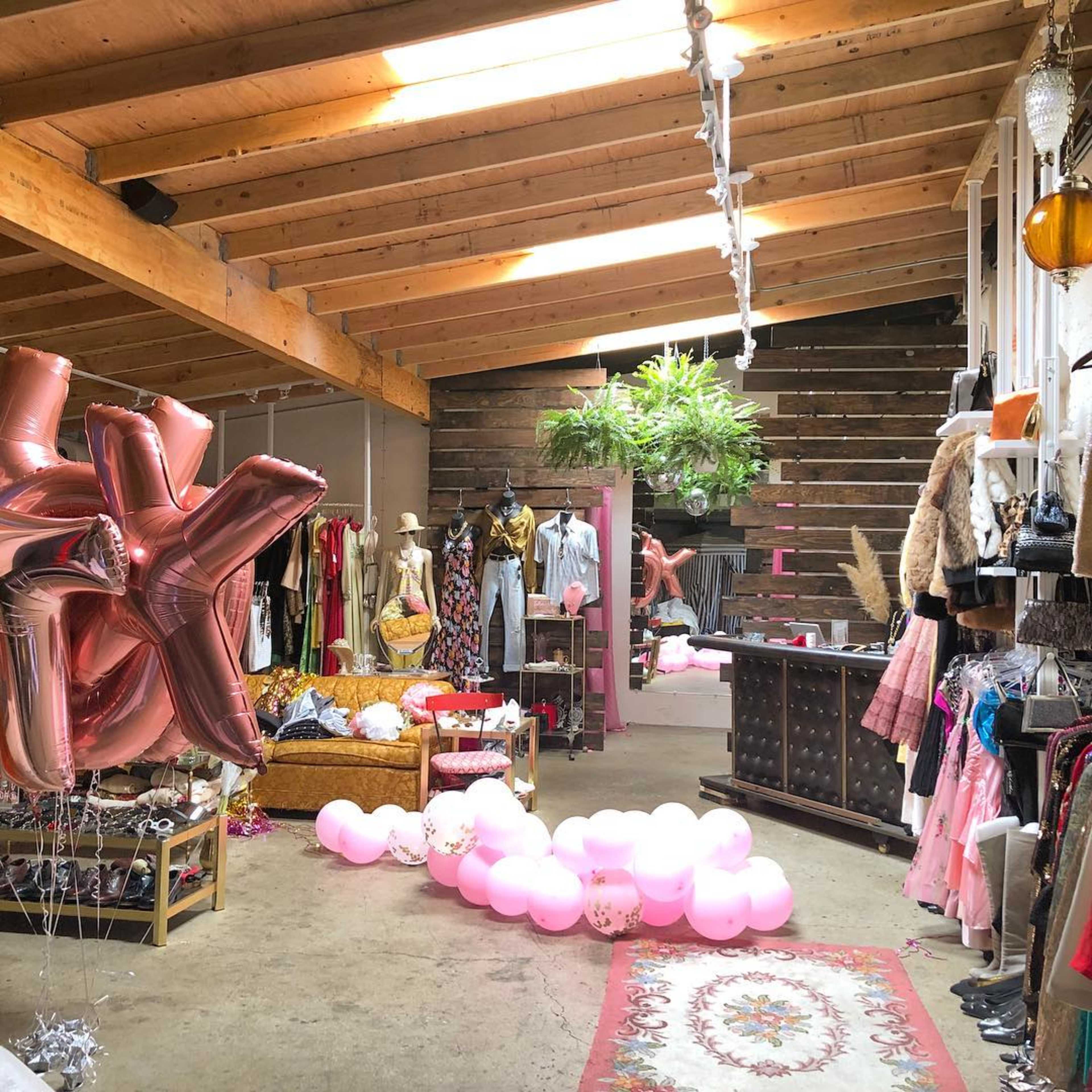 A spacious boutique features clothing racks, decorative balloons, and wooden beams overhead.