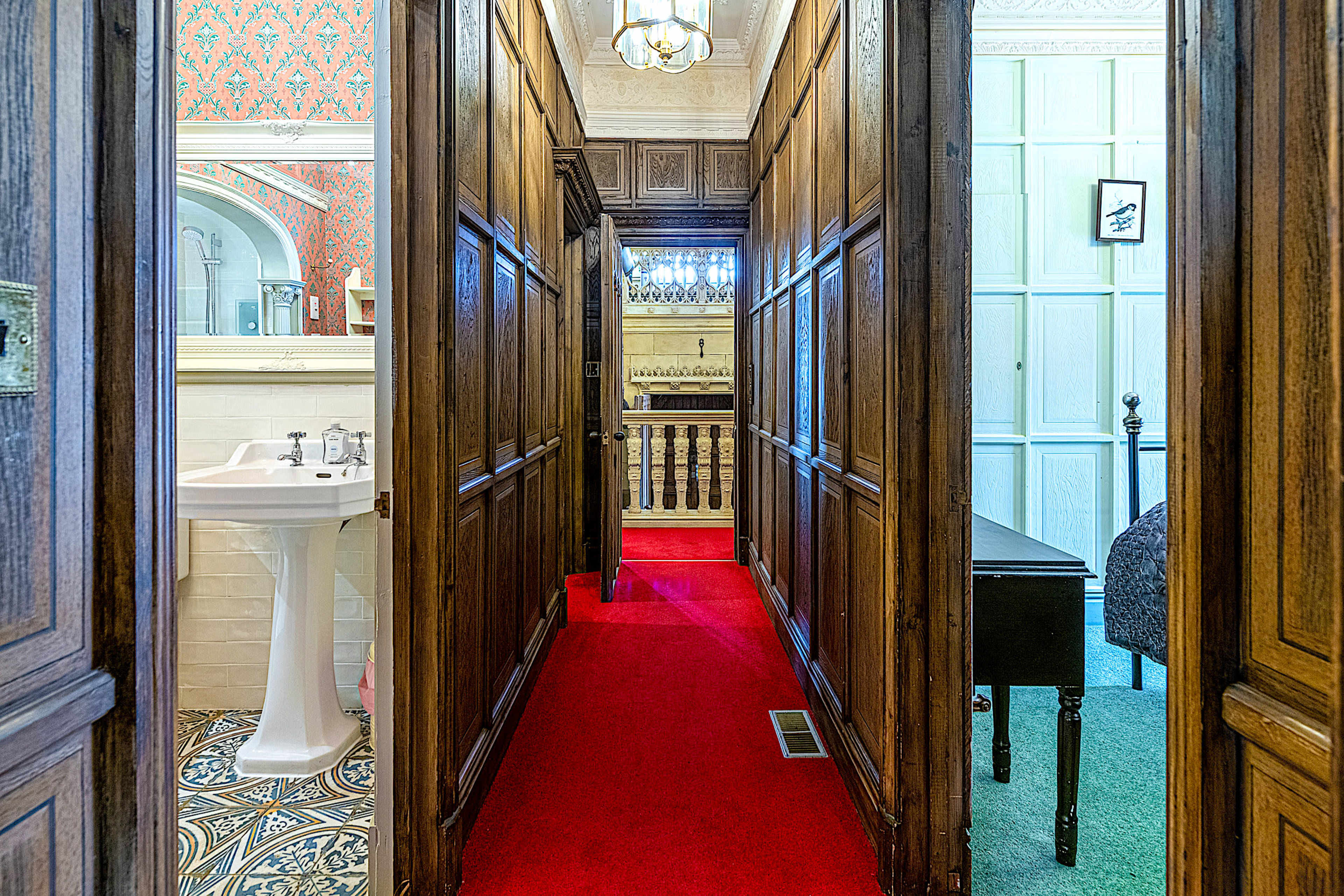 The image shows a hallway lined with wooden panels, featuring a red carpet leading to rooms with ornate decor and patterned tiles.