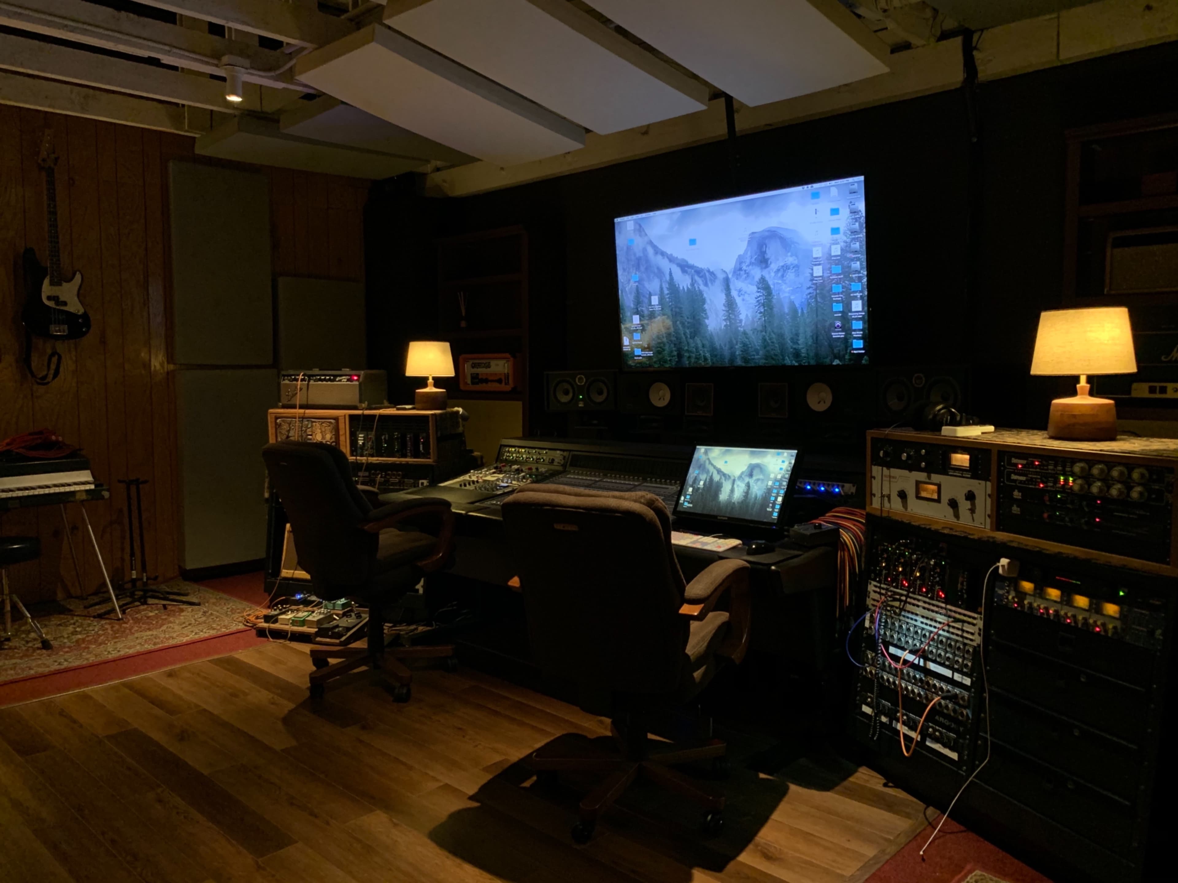 A music recording studio featuring a large screen, mixing console, and various audio equipment in a dimly lit room.