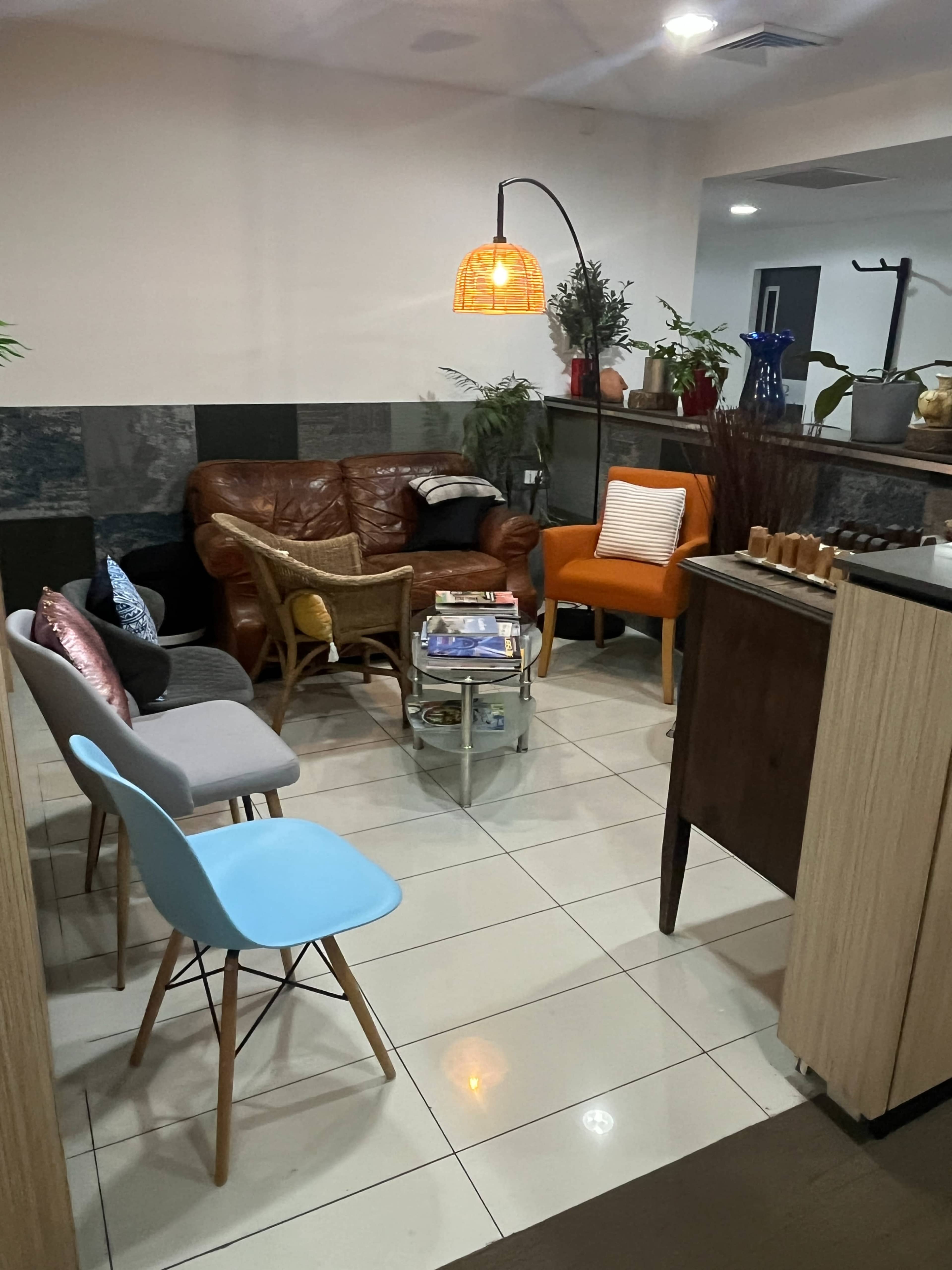 The image shows a cozy seating area with a mix of chairs and a leather couch, surrounded by plants and decorative items.